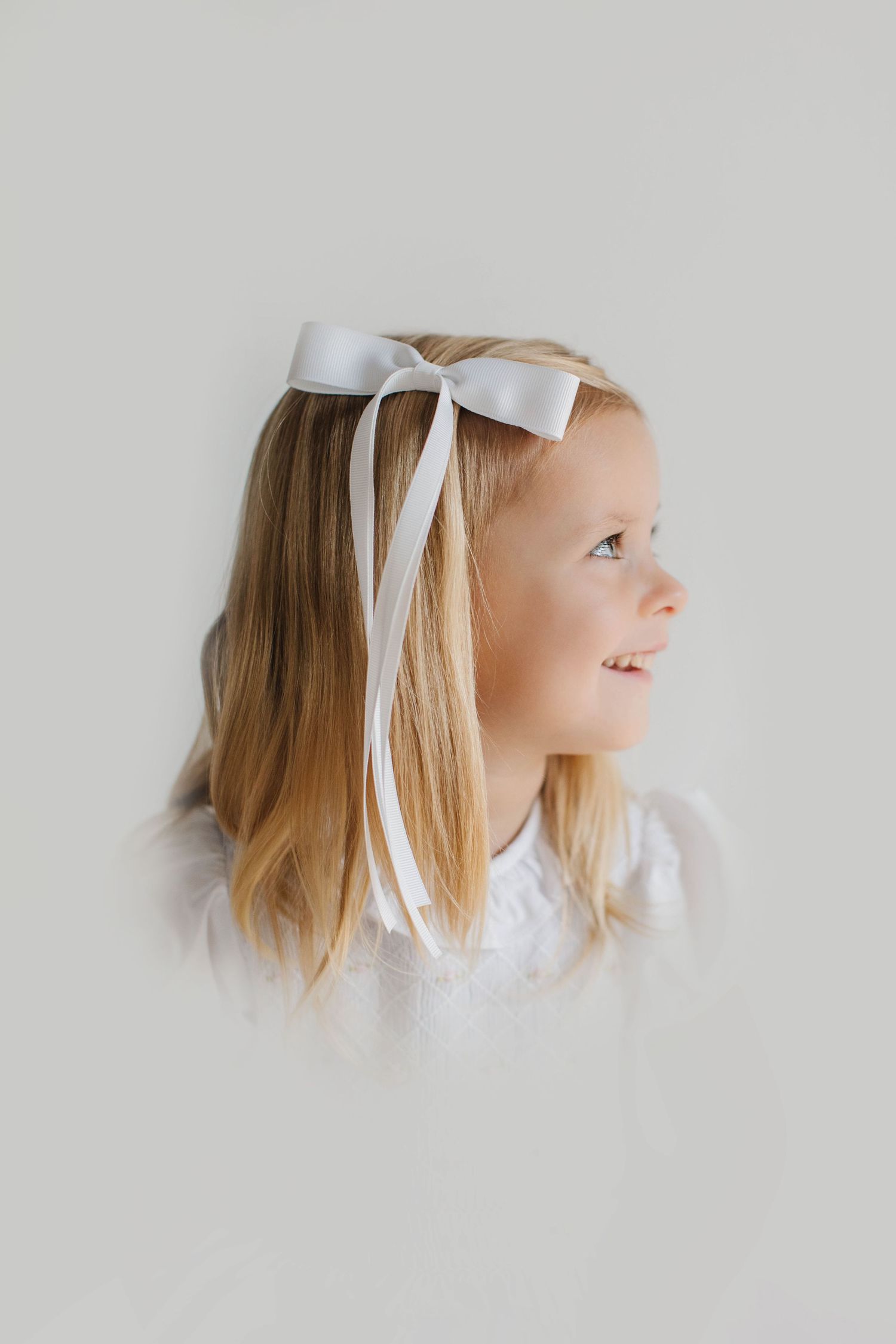 Side profile views with white bow and blonde hair against minimal gray background.