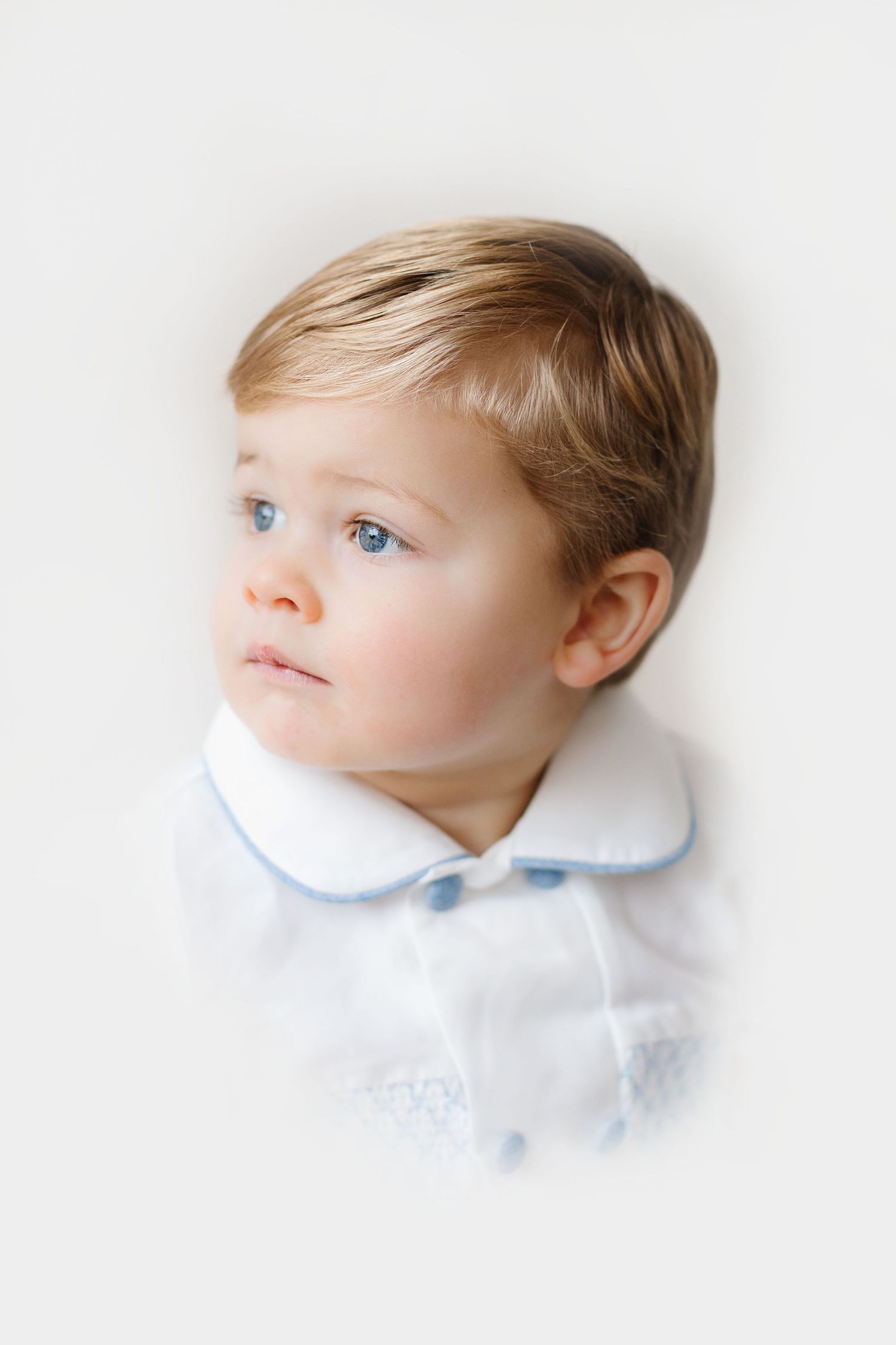A young child in a white collared shirt gazes thoughtfully to the side against a light background.