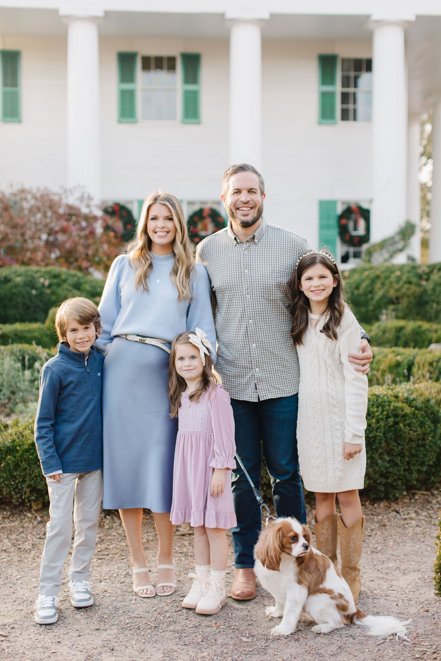A family poses together on a garden path with their brown and white spaniel dog in three similar outdoor portraits.