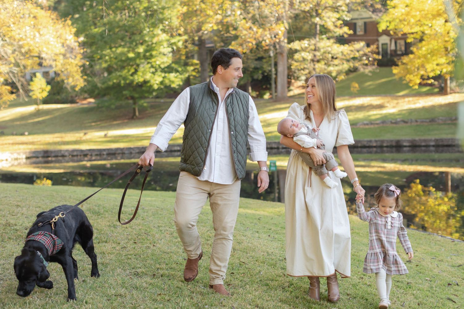 A family walks together in a sunlit park during autumn with golden foliage in the background.