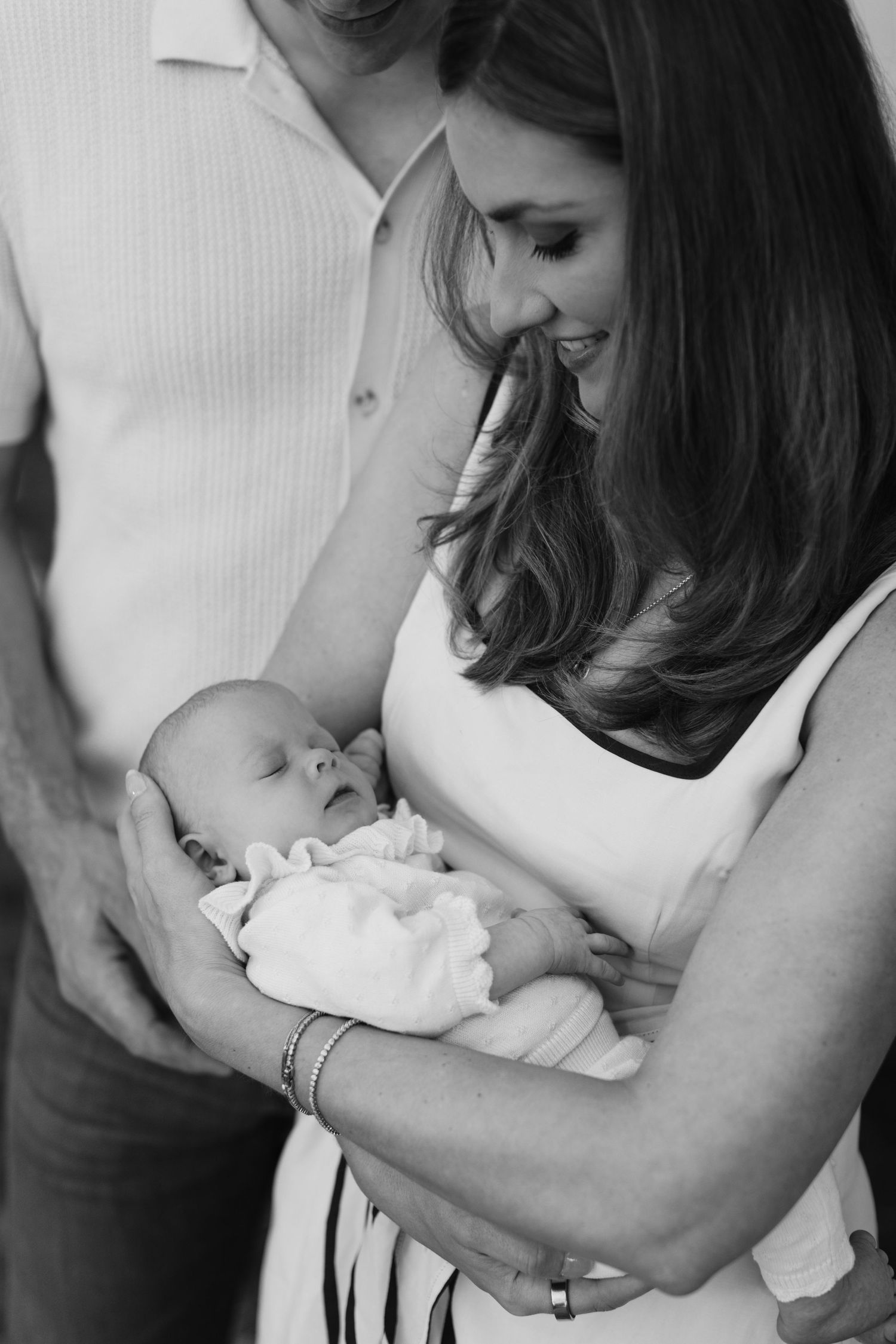 Black and white photo of parents lovingly gazing at their sleeping newborn baby.