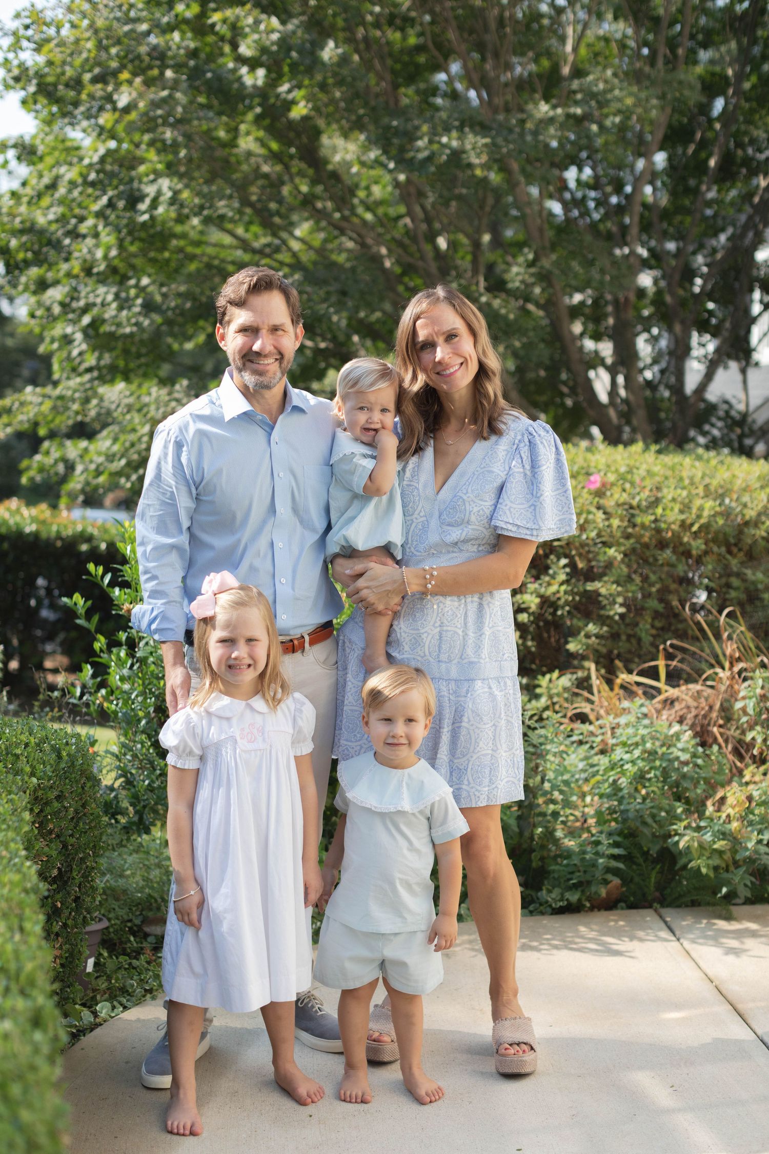 Family enjoys a sunny summer day together in a garden setting with coordinated light blue and white outfits.