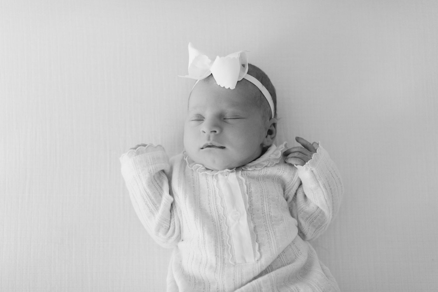 A sleeping baby wearing white clothing lies on a light colored background in a peaceful pose.