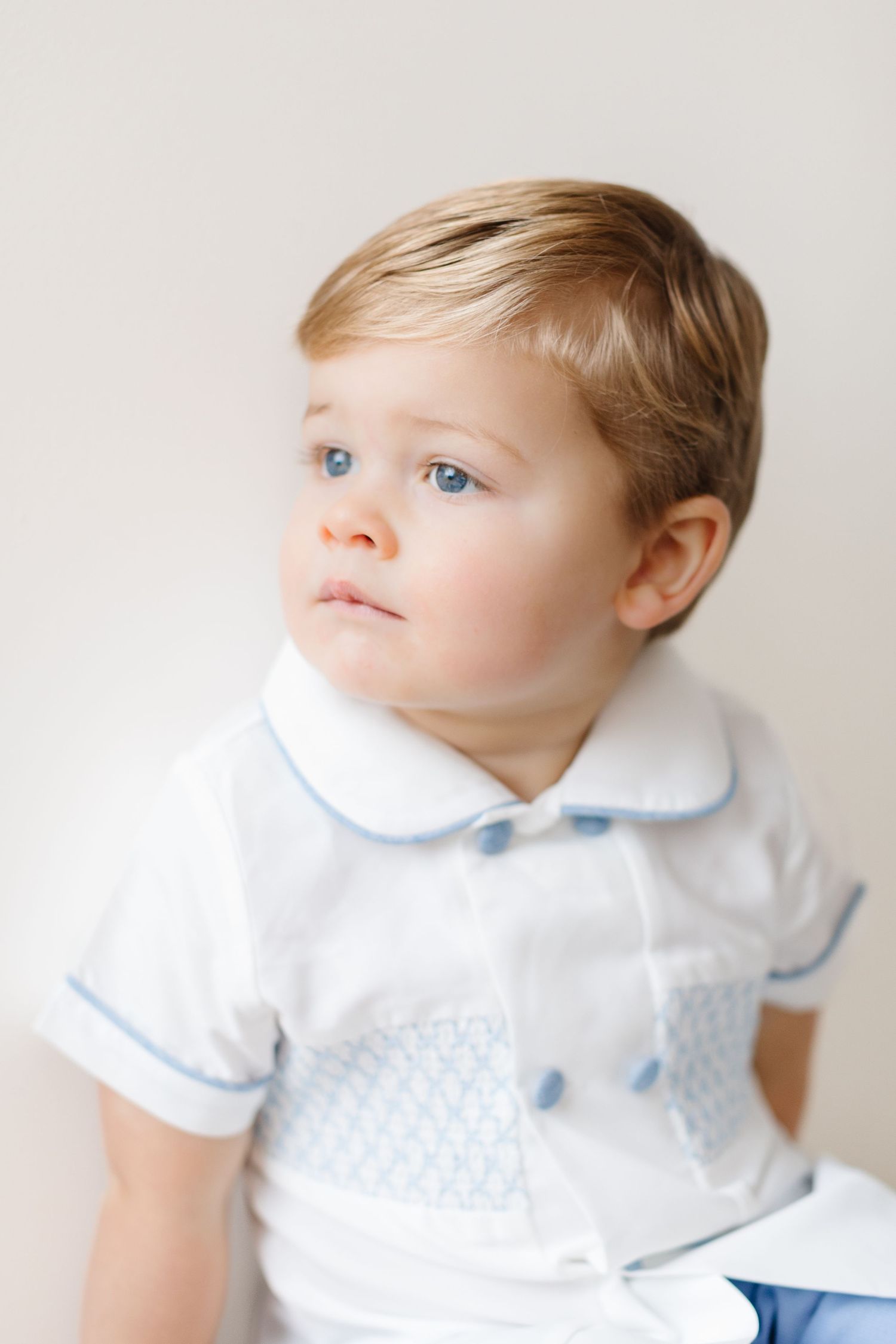 A young child in white clothing with blue accents gazes upward against a light background.