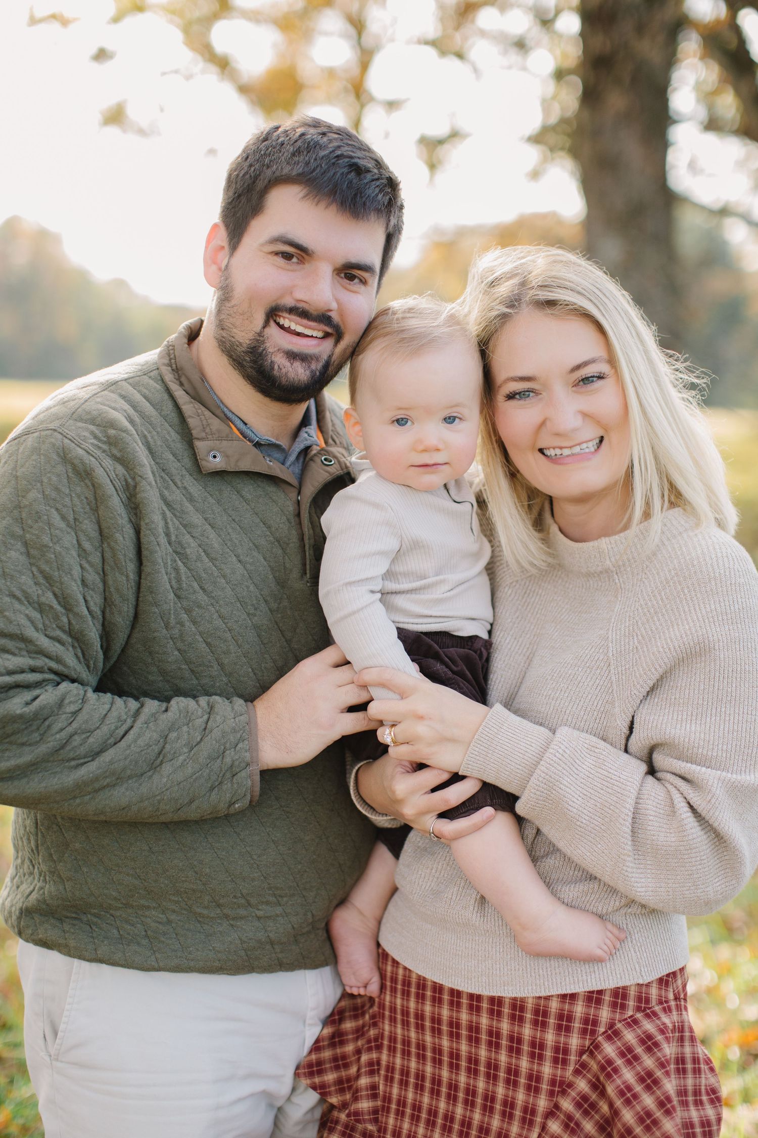 A family poses together outdoors during autumn wearing cozy sweaters and warm smiles.