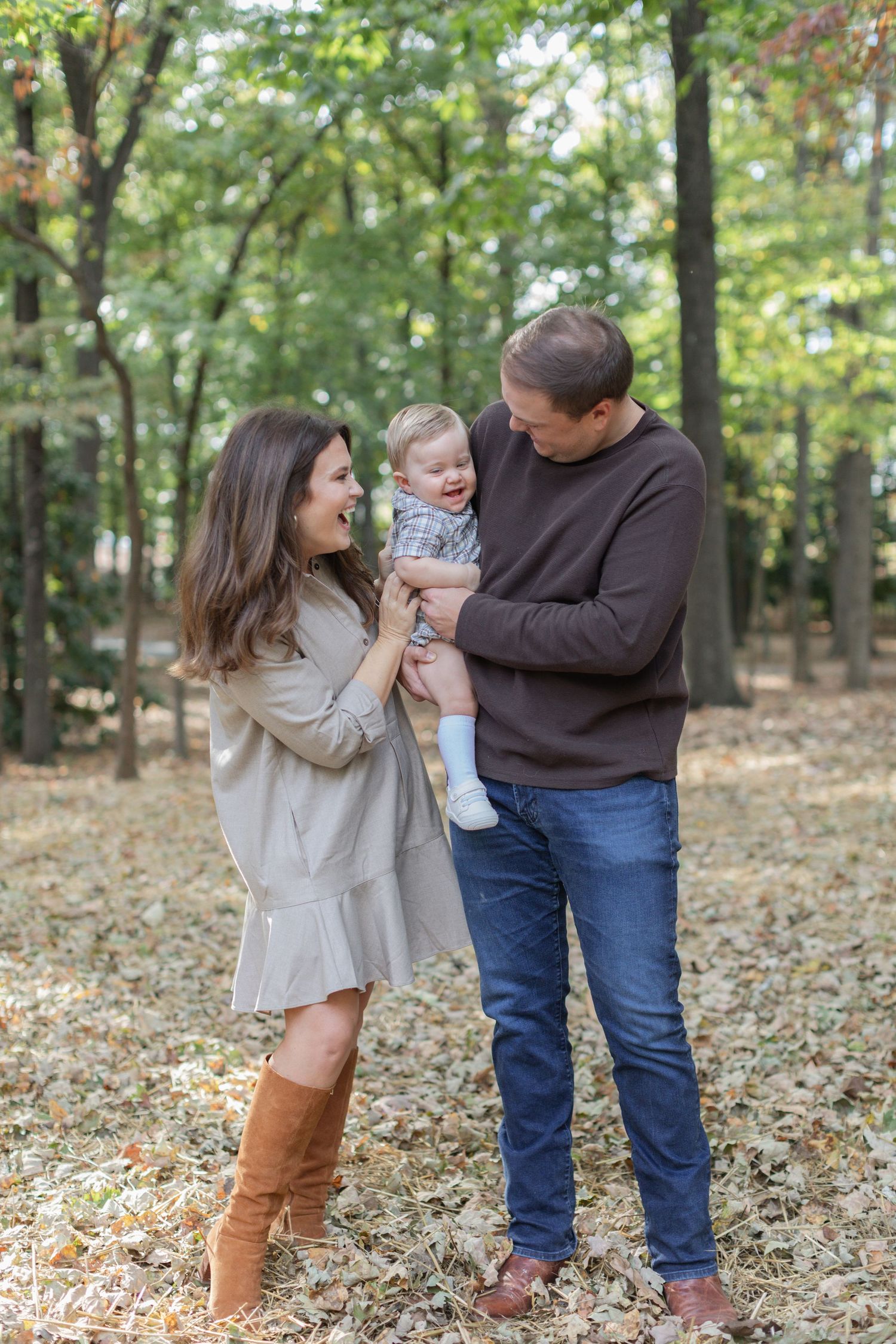 A family plays together in autumn leaves at a park while wearing casual clothing and boots.