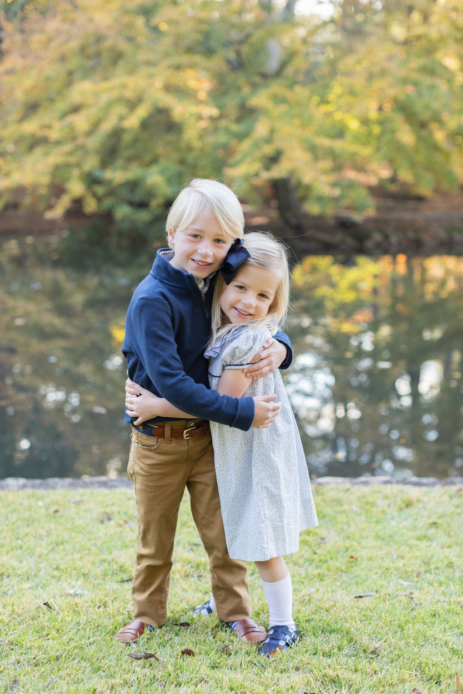 Two young siblings hugging and playing together on a grassy hill during a fall afternoon.