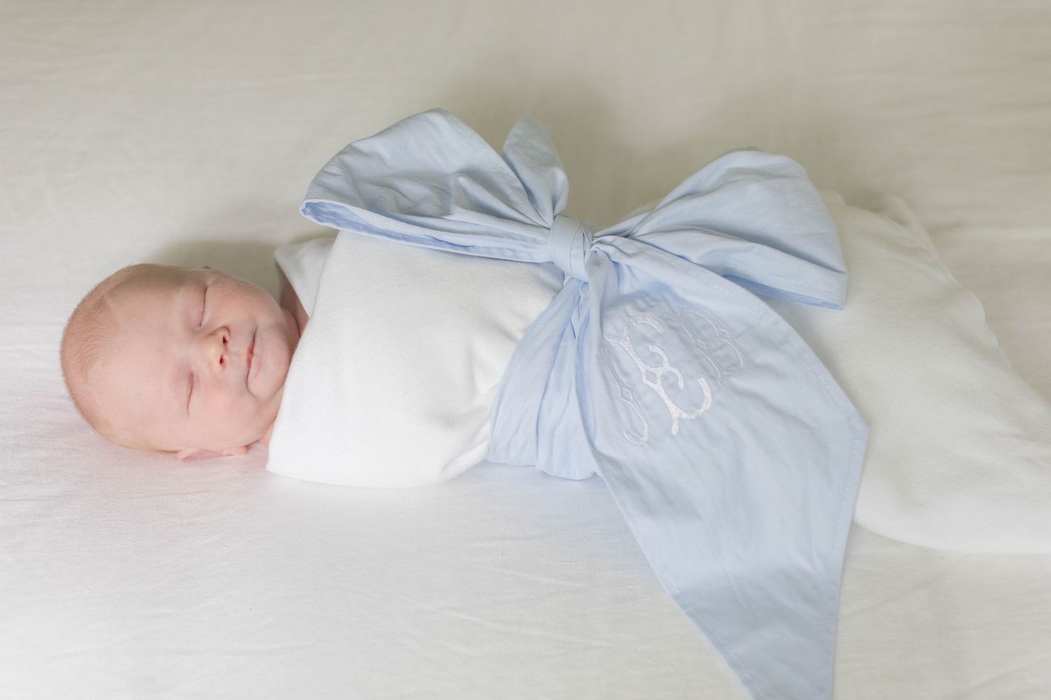Baby in light blue sleepwear lying on white bedding in soft natural light.