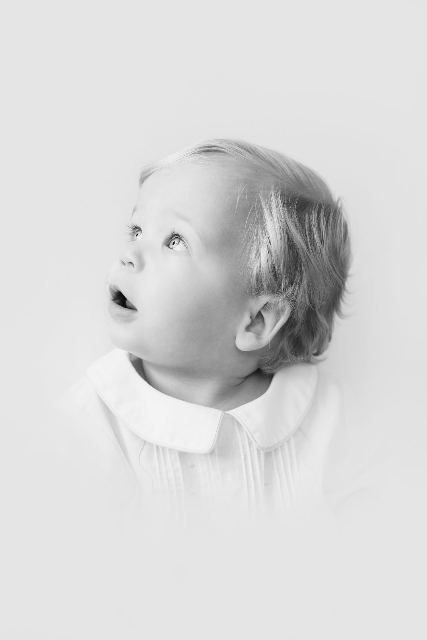 Black and white portrait of a young child looking up with an expression of wonder and curiosity.