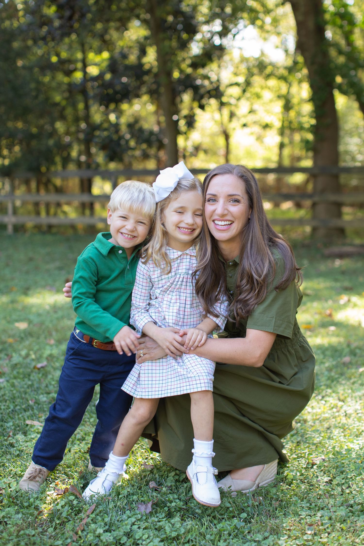 A family group poses together on grass in a sunlit outdoor setting wearing coordinating green outfits.