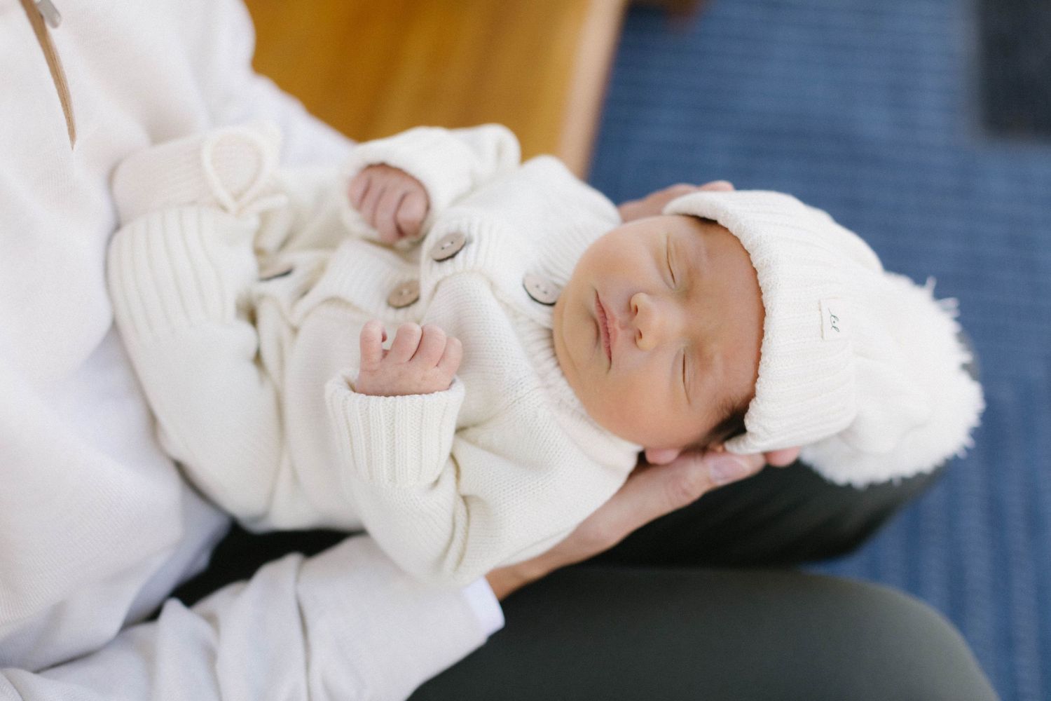 A sleeping newborn baby dressed in white with a matching cap rests on cozy white fabric.