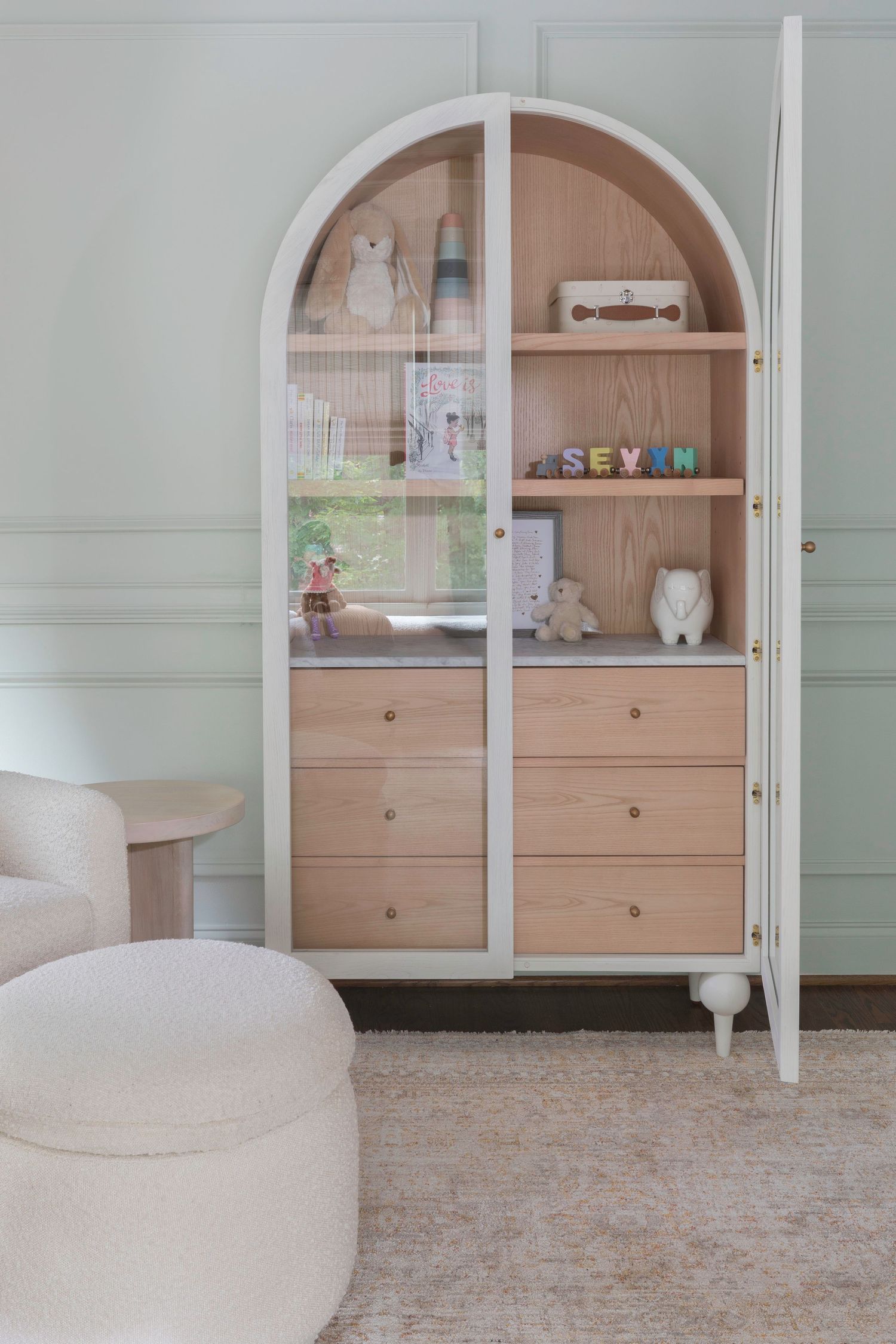 Modern arched nursery cabinet with wooden drawers and decorative shelving in cream tones. Atlanta Interior Design Photography