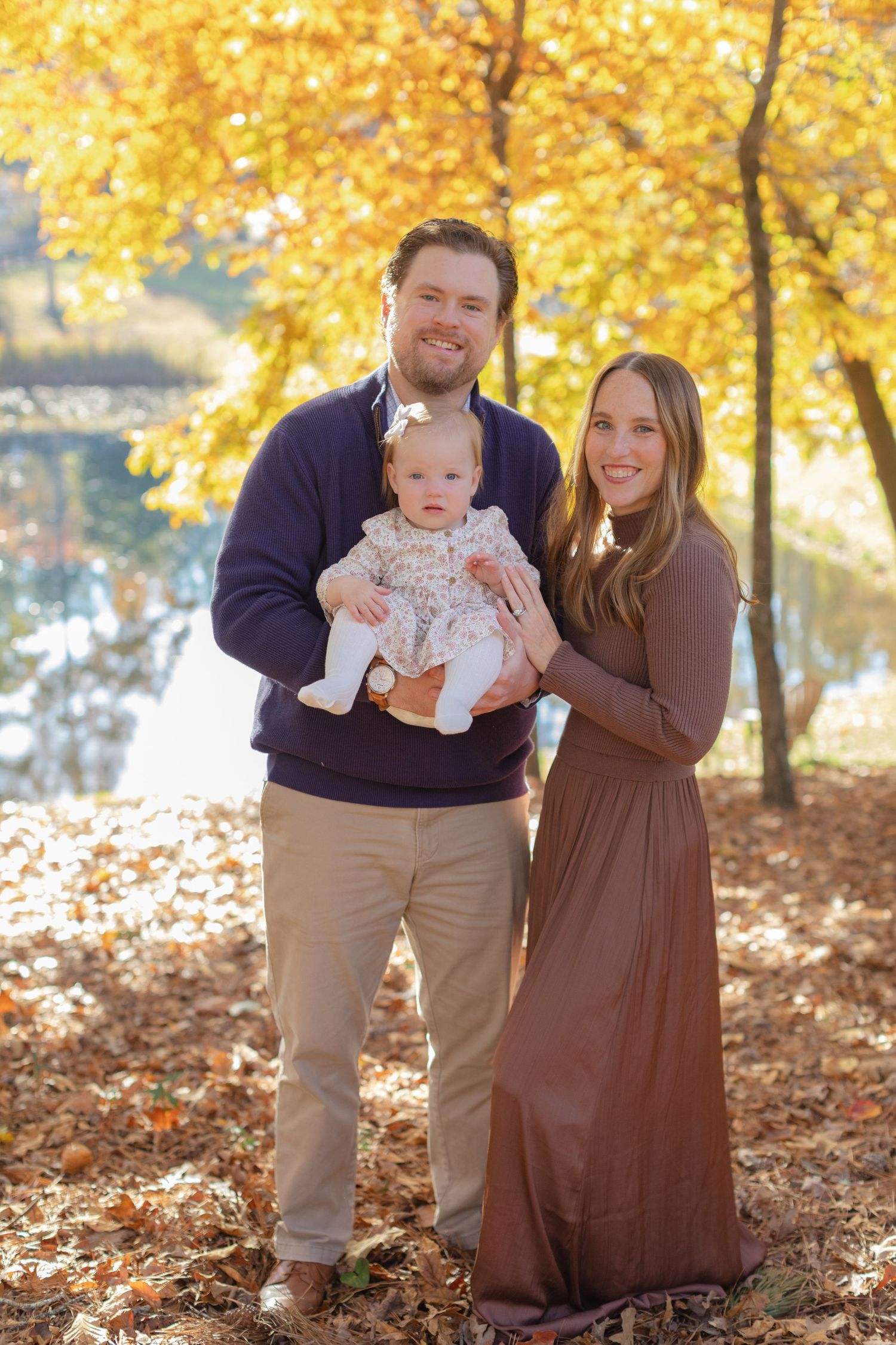 A family poses together on fallen autumn leaves with golden trees in the background during a fall photoshoot.