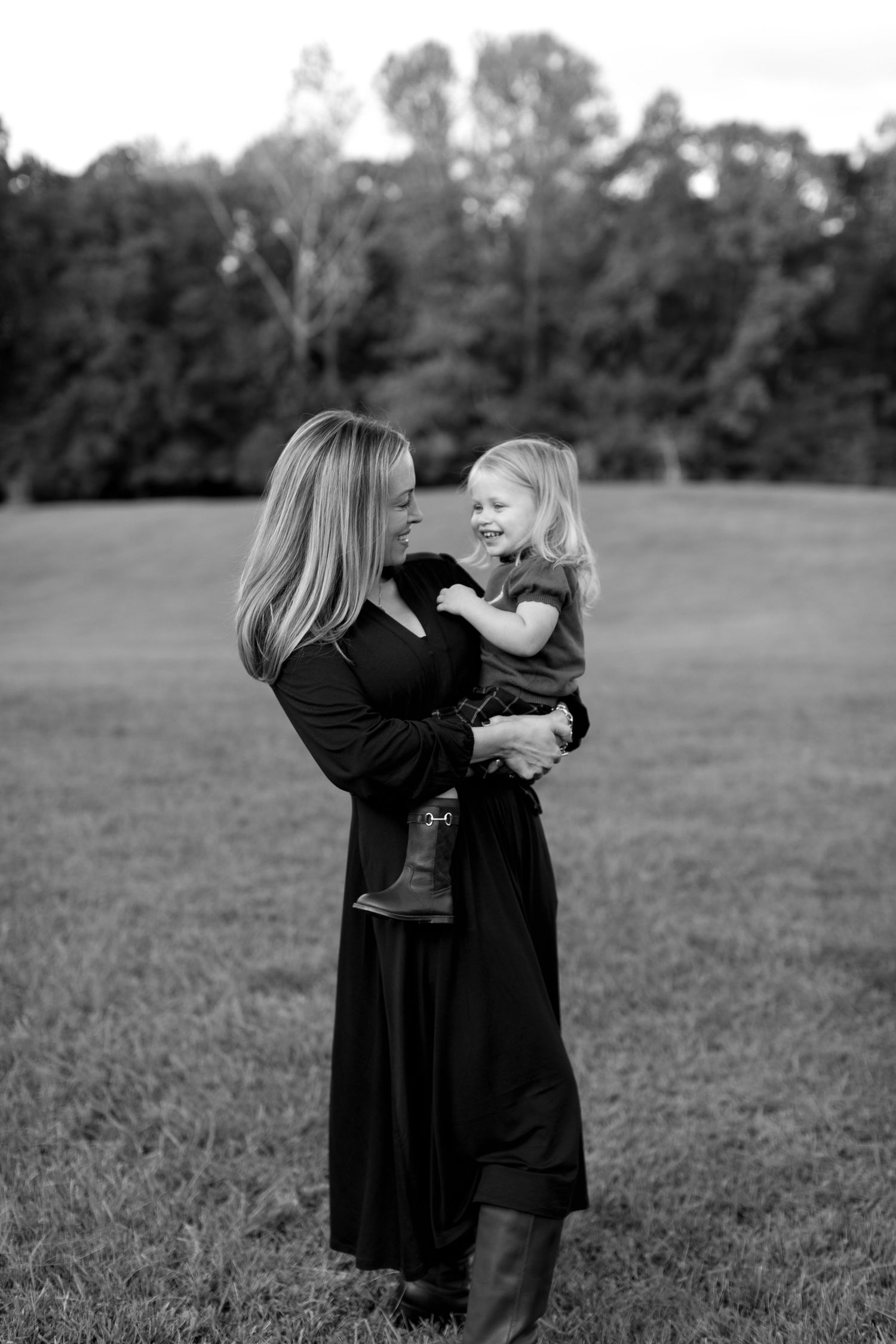 Two figures in black dresses embrace while standing in a grassy field.