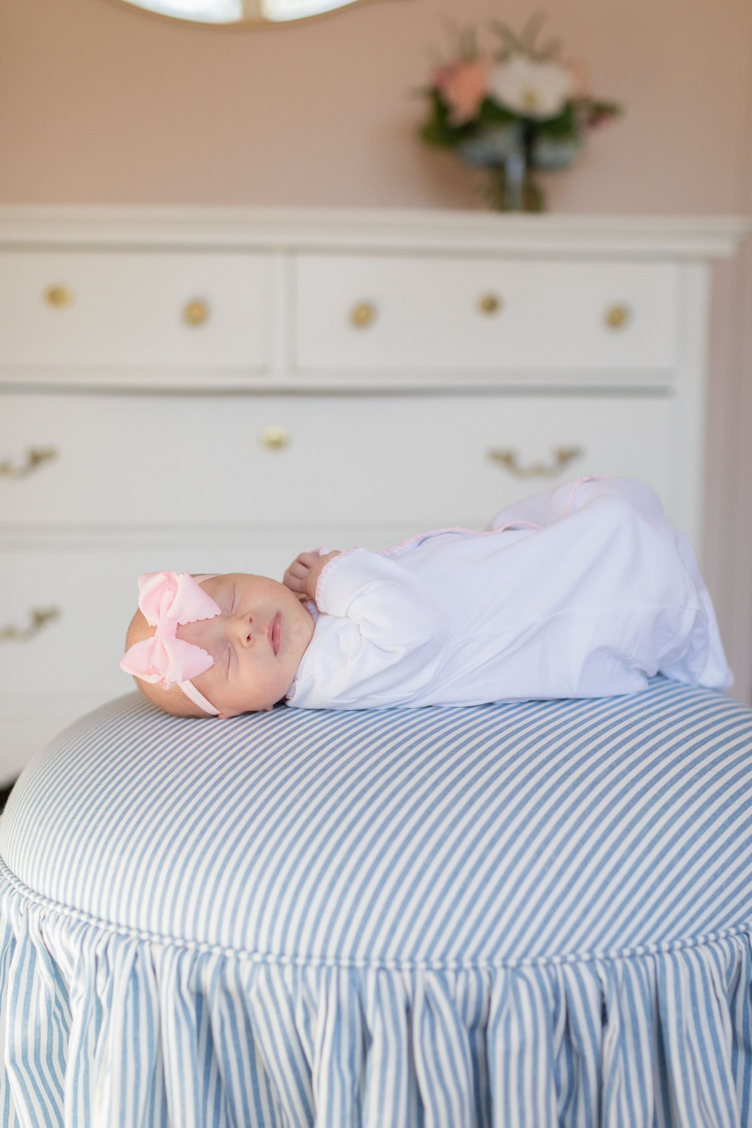 A sleeping newborn baby wearing a pink bow rests on a blue and white striped cushion.