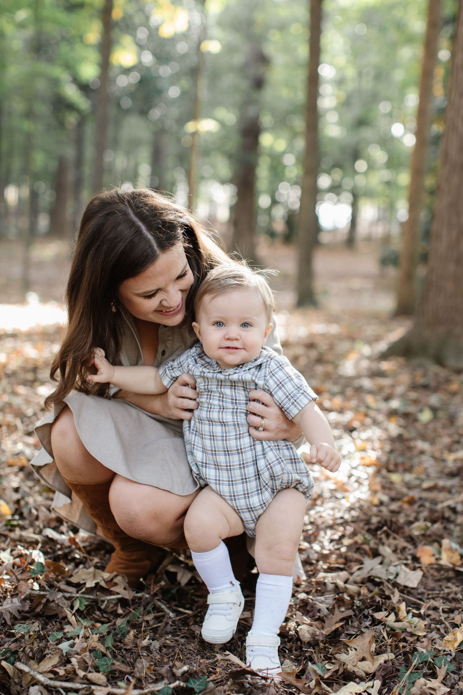 A tender outdoor portrait in a wooded setting with autumn leaves scattered on the forest floor.