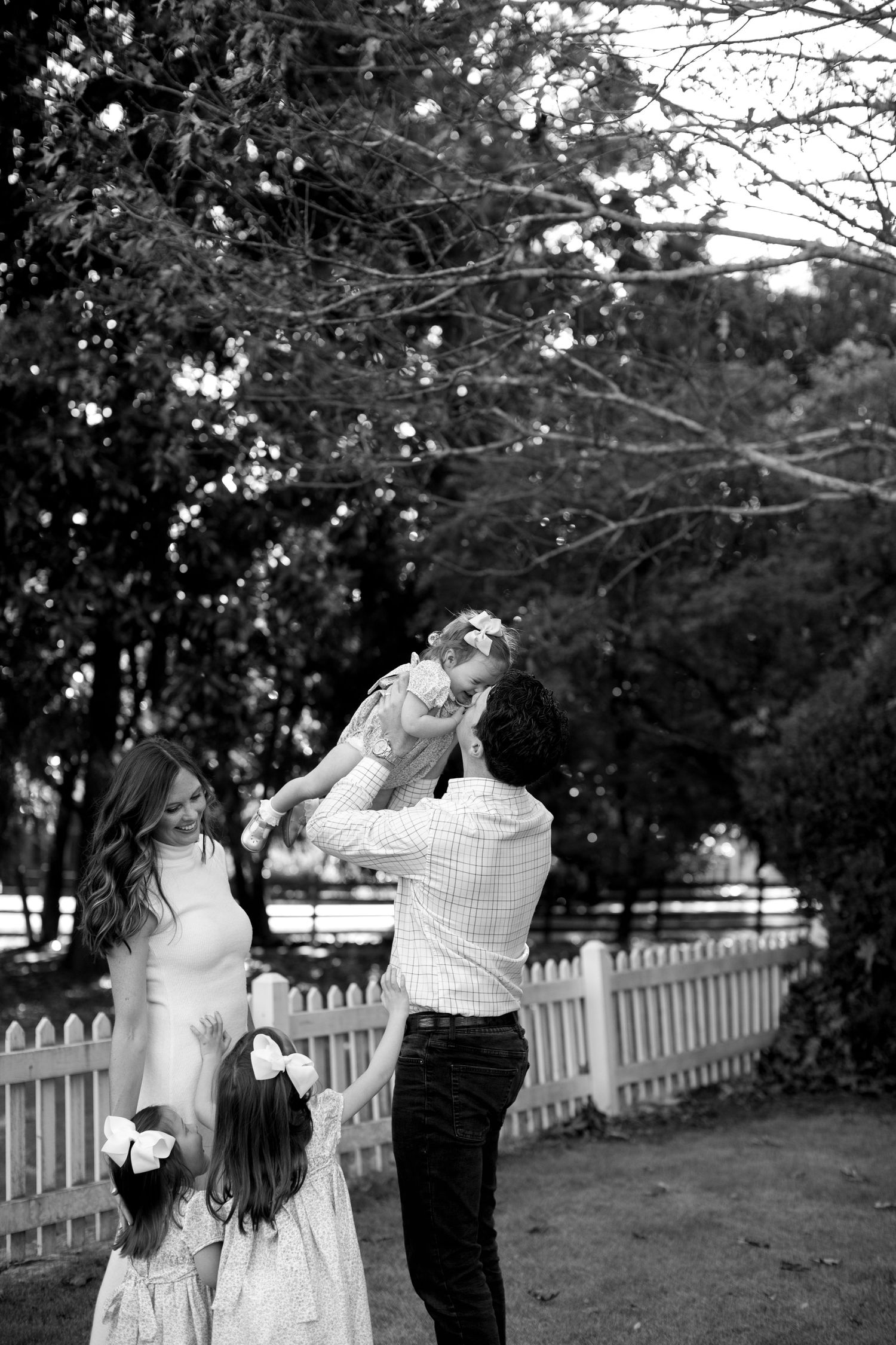 A couple dances playfully in a garden setting with a white picket fence and trees in the background.