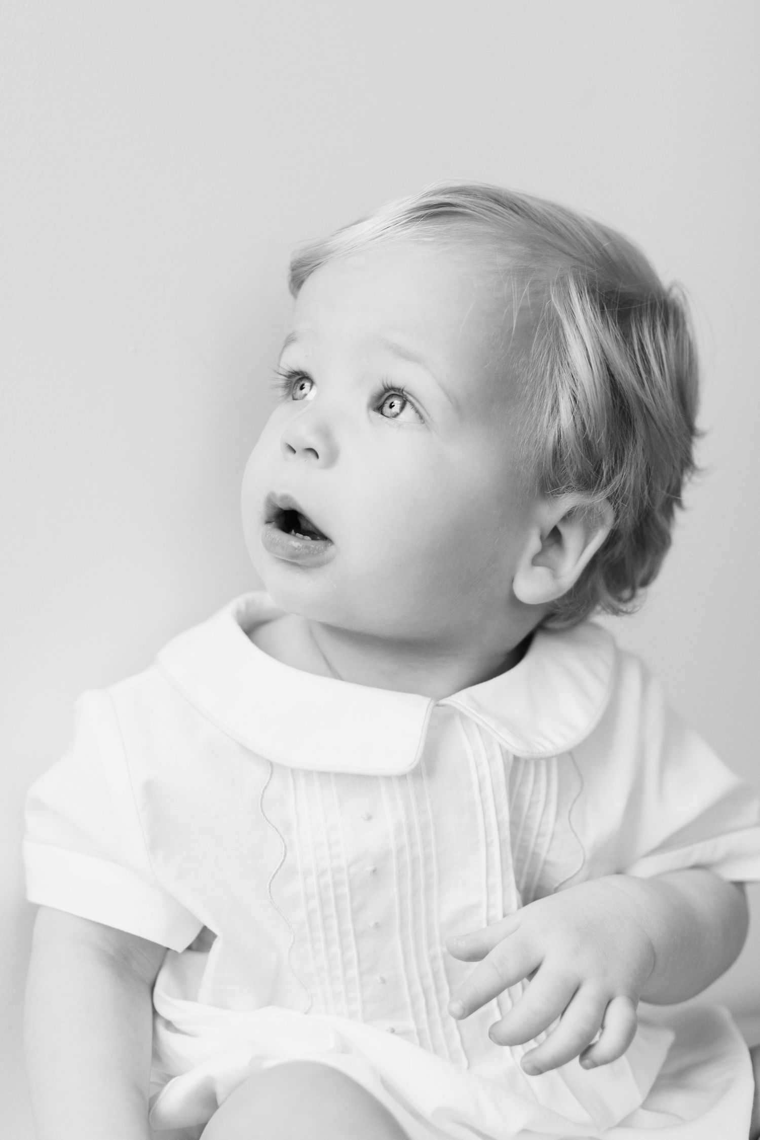A baby in white clothing gazes upward with wonder in this black and white portrait series.