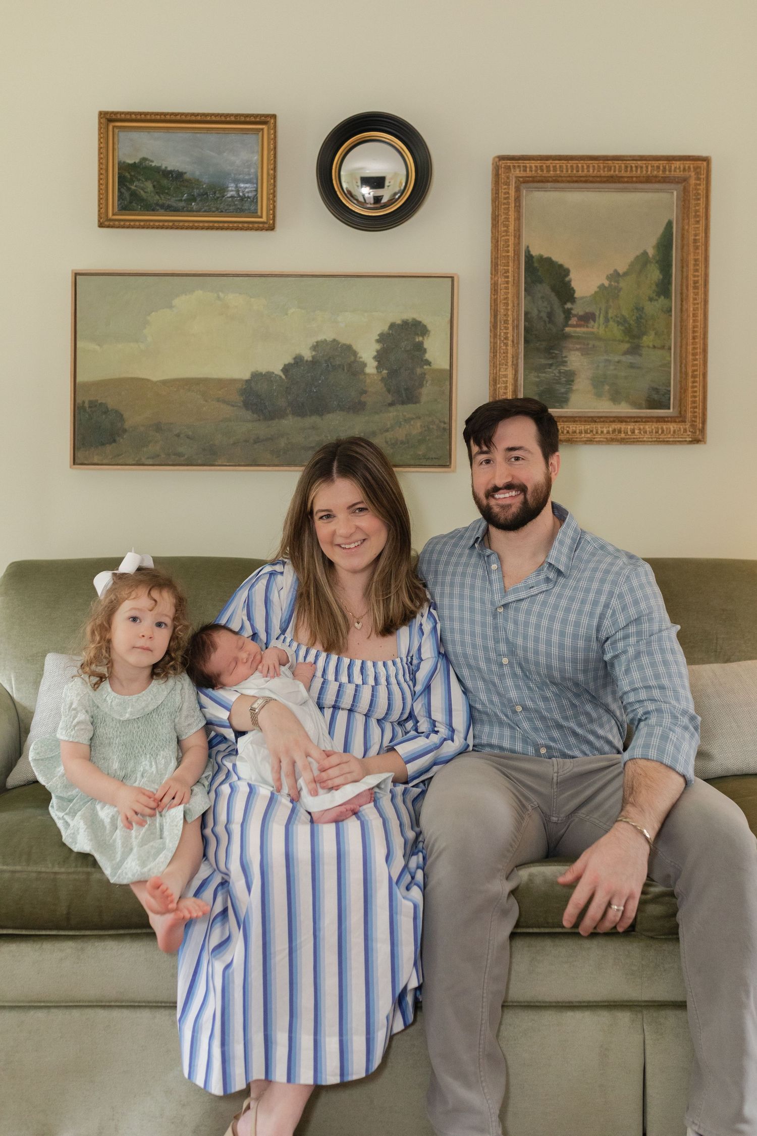 Family relaxing together on a couch with landscape paintings on the wall behind them.