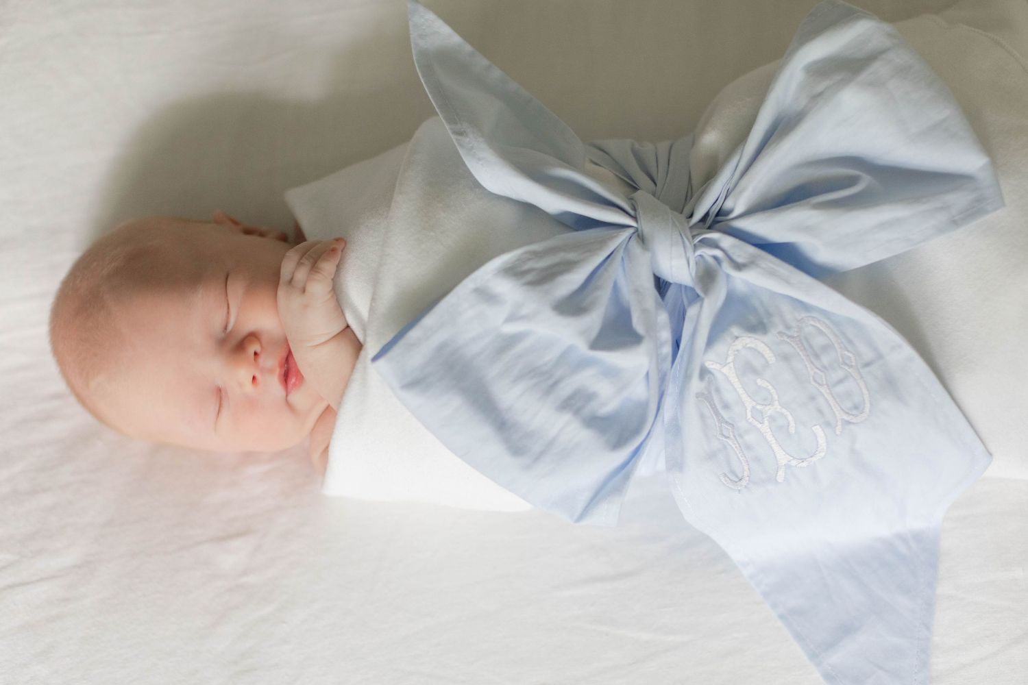Artistic newborn photography with baby wrapped in light blue fabric against white bedding.