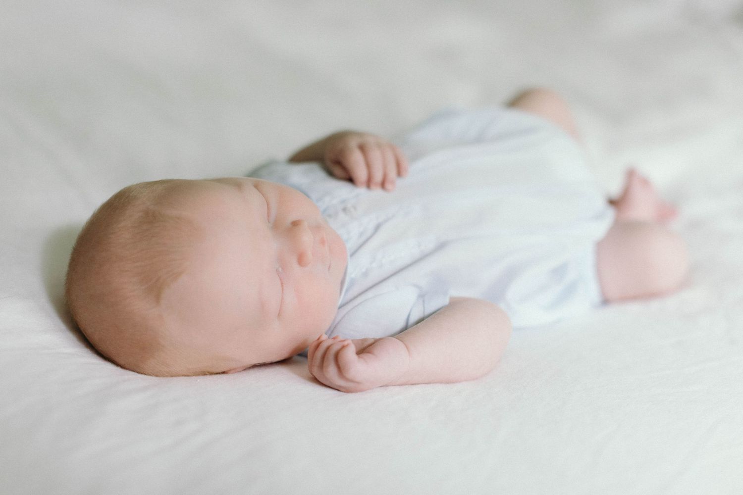 Peaceful newborn baby sleeping on white sheets in a bright room.