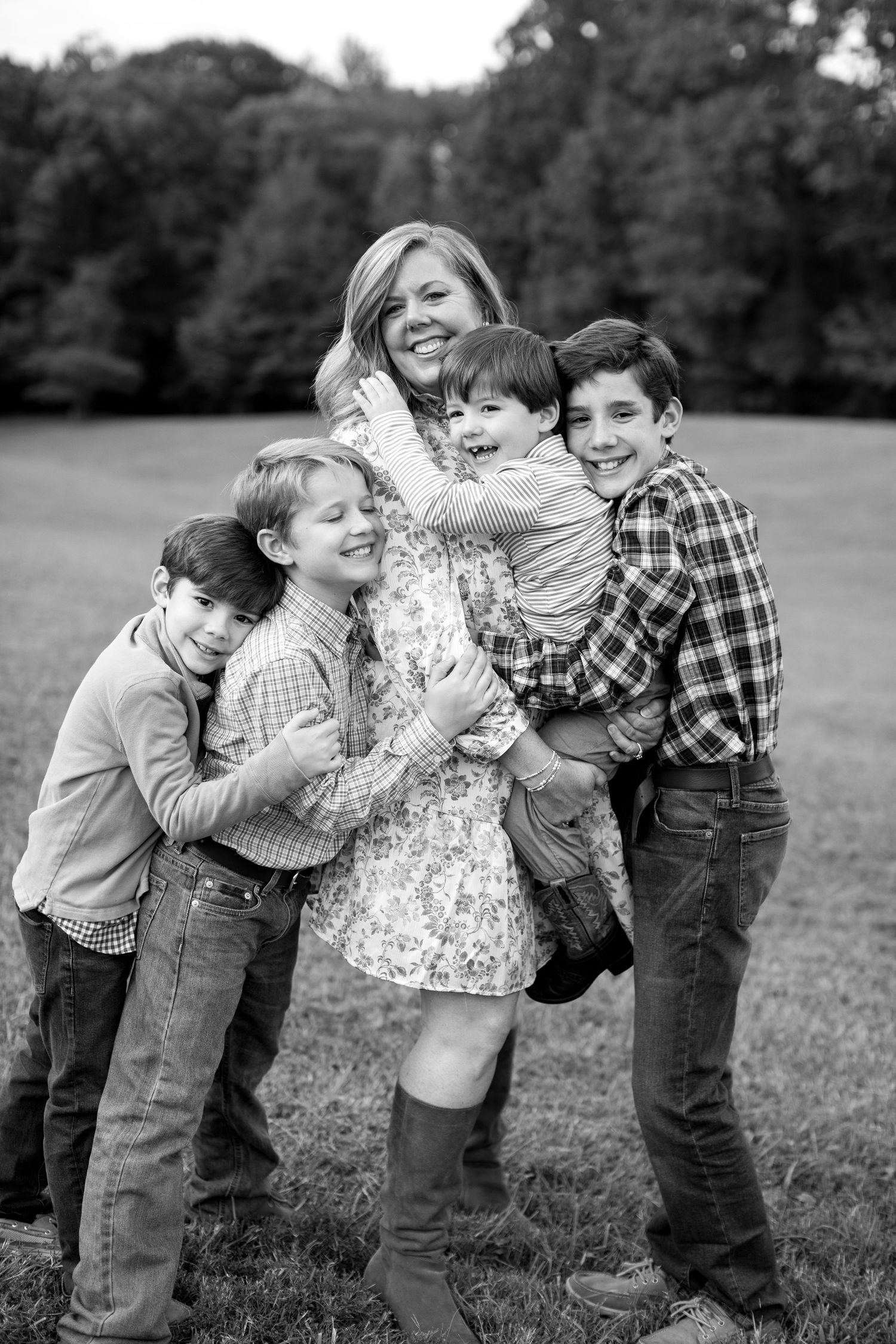 A joyful black and white portrait of a family embracing and laughing together outdoors in a grassy field.