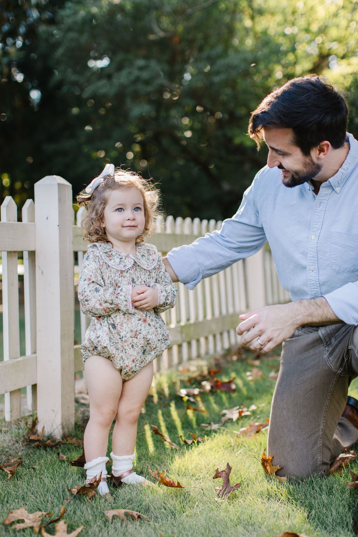 A series of candid outdoor photos showing tender moments between parent and child by a white picket fence in sunlight.