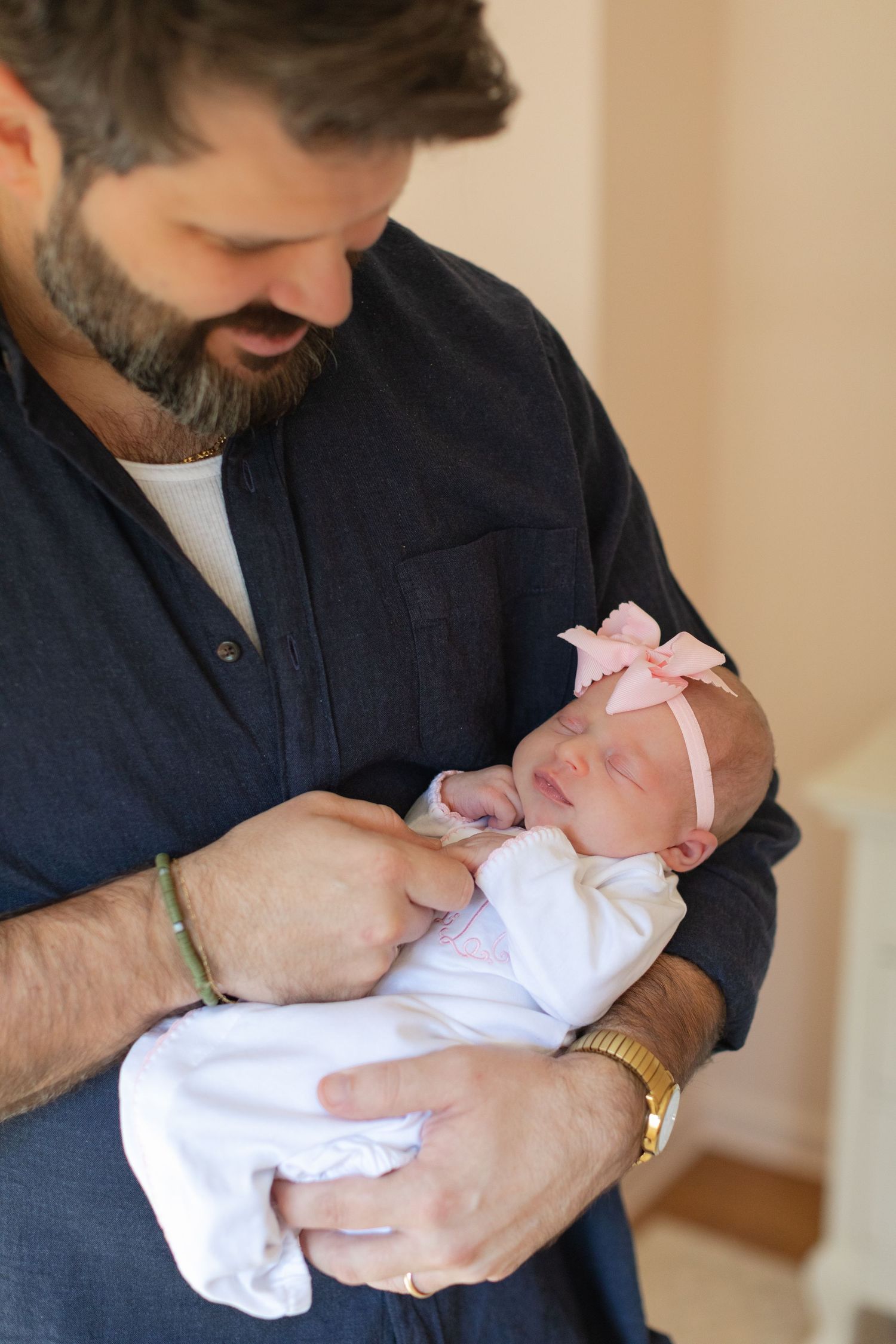 Parent in navy shirt tenderly holding sleeping newborn wearing pink bow.