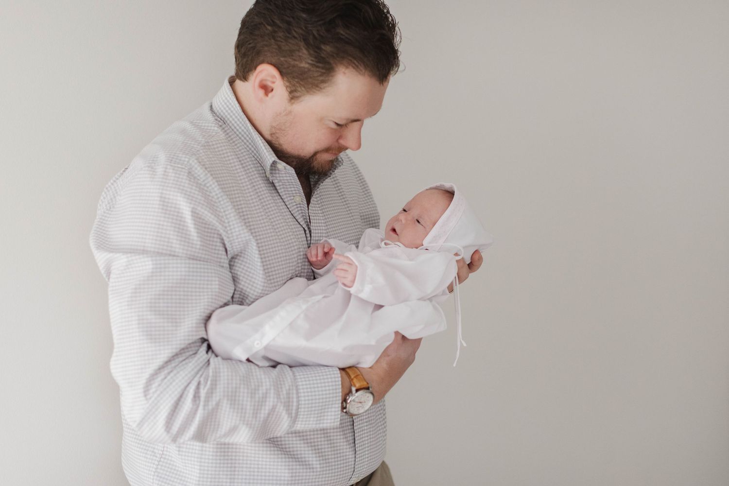 Parent in light colored shirt holding and gazing at sleeping newborn.
