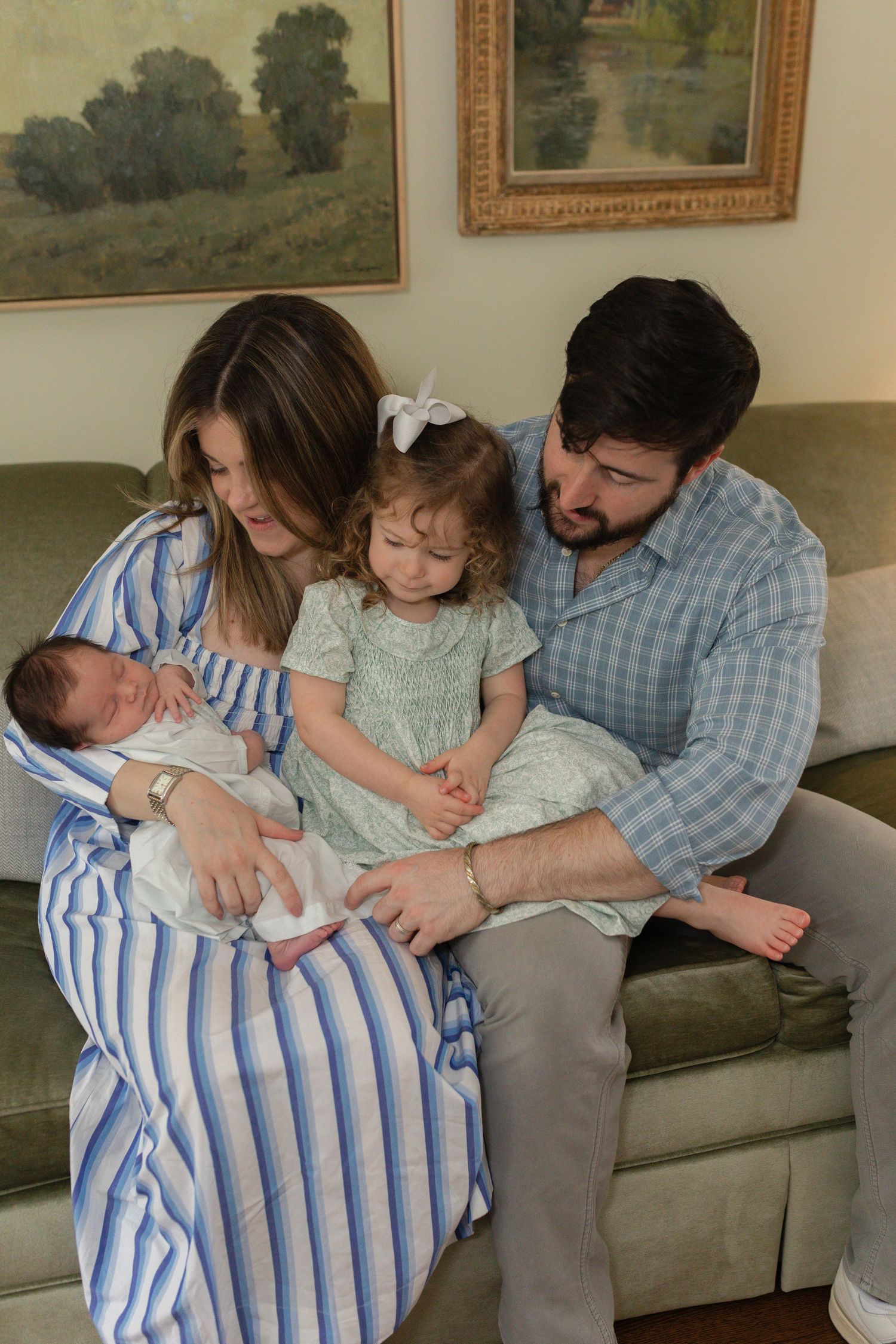 A tender family moment on a green couch with a newborn baby and toddler.