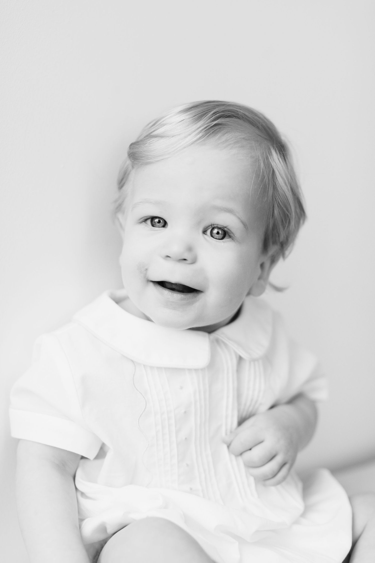 Close-up black and white portrait of a baby in white clothing showing different expressions.