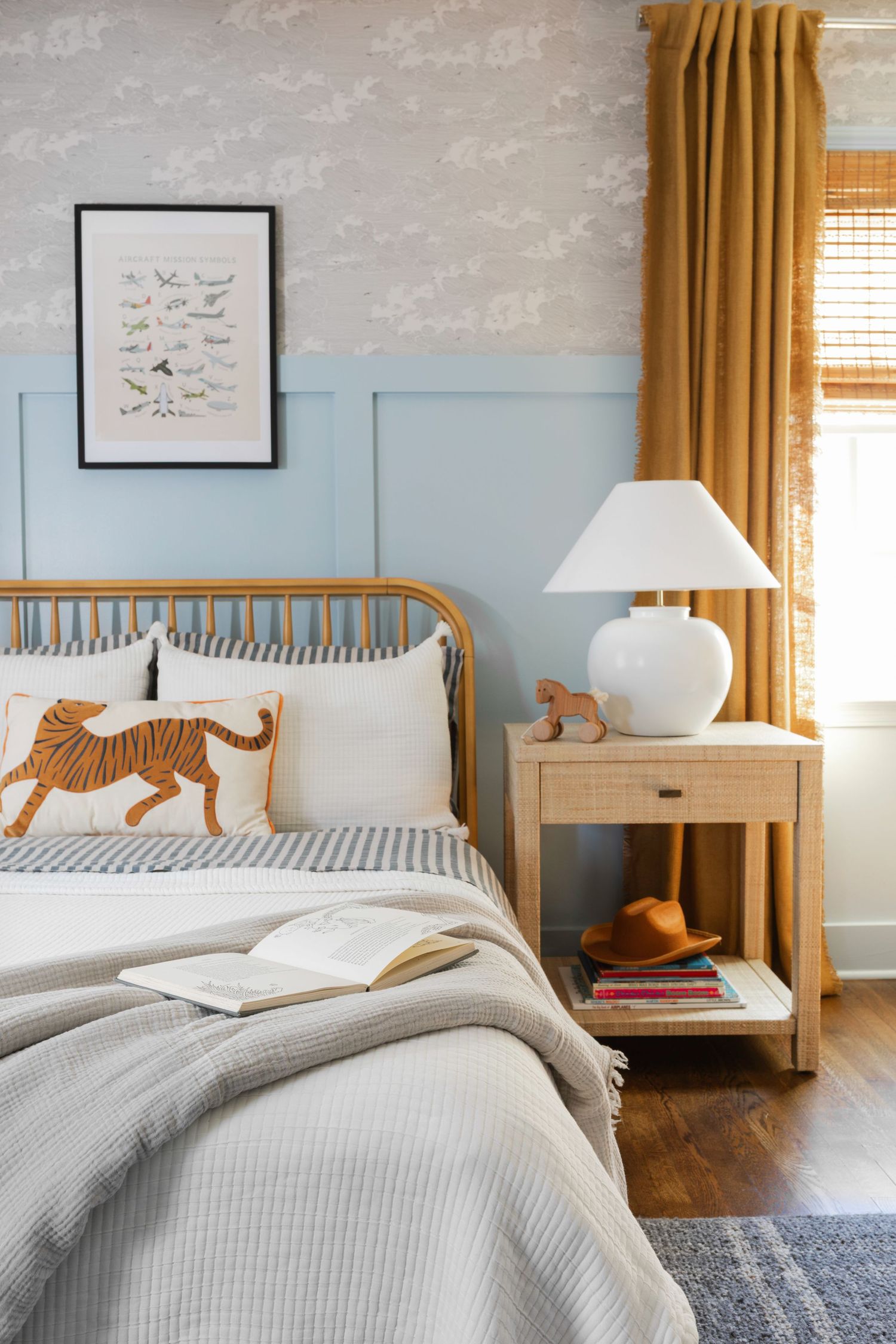 A cozy bedroom with blue-gray walls features mustard curtains, wooden floors, and minimalist decor with tiger artwork.
