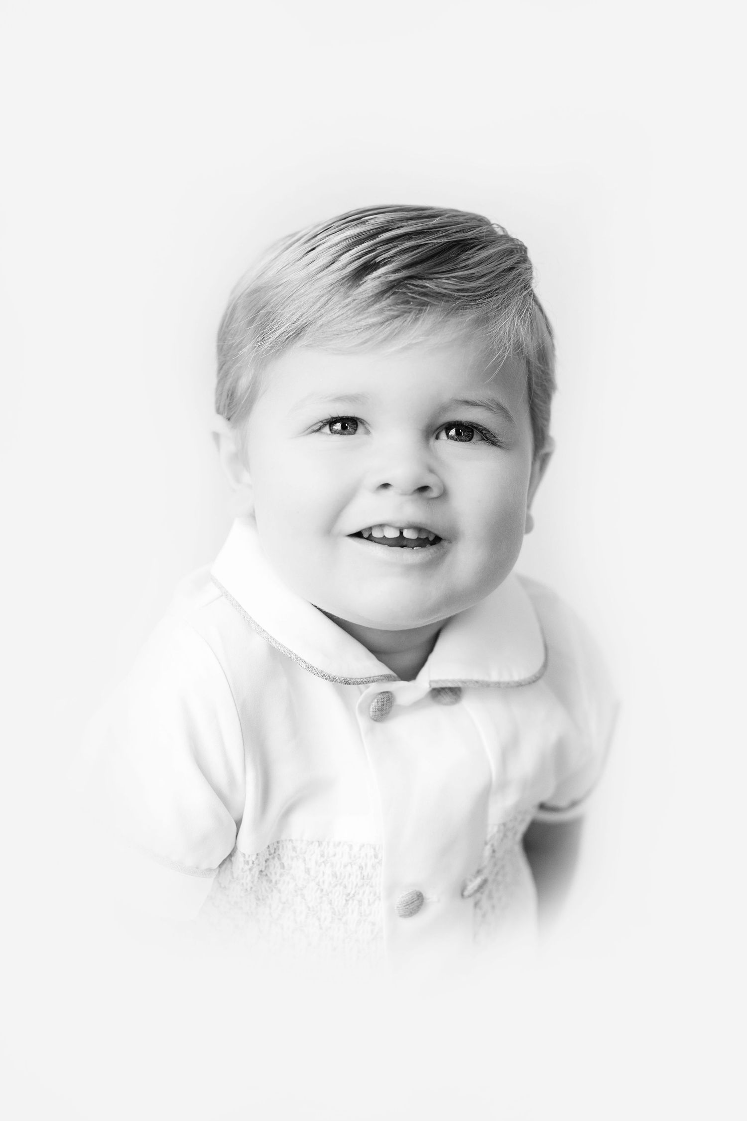Three black and white portraits of a young child with a sweet smile wearing white against a light background.