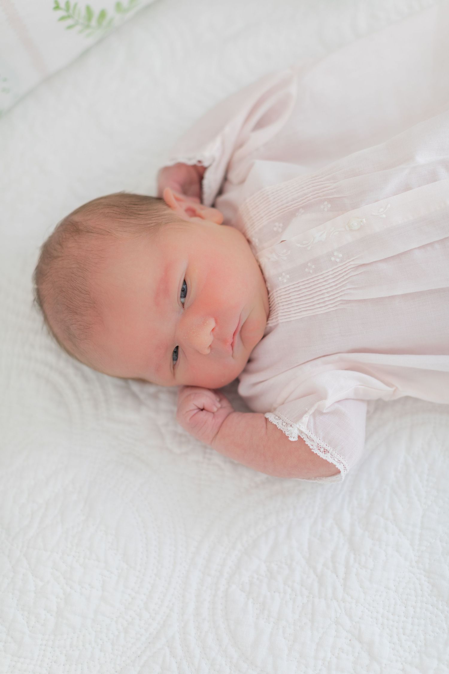 A newborn baby wrapped in white fabric lies on a textured white blanket in a series of peaceful poses.