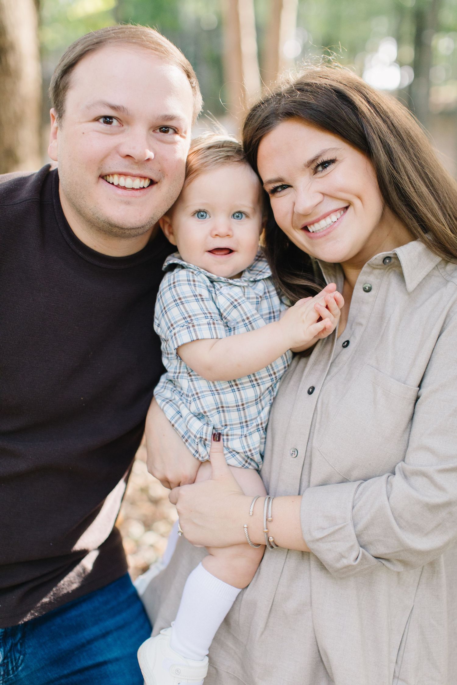 A family poses together outdoors, wearing casual attire and smiling warmly at the camera.