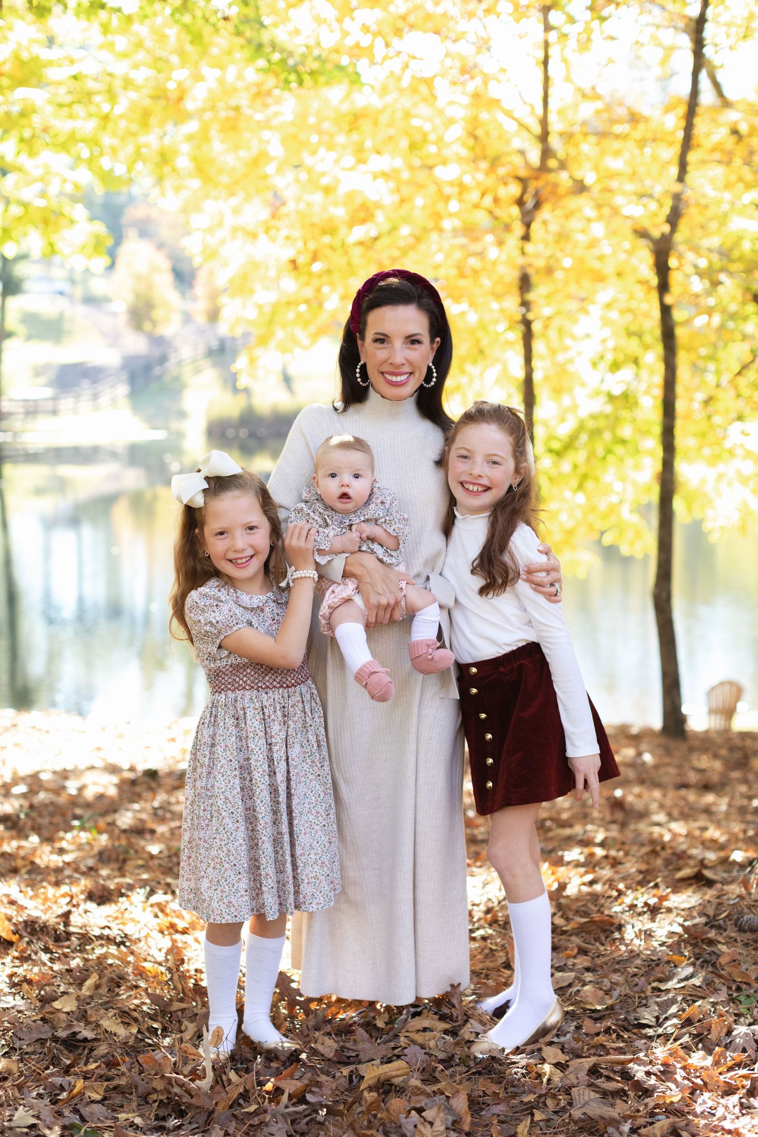 Three young children pose together in autumn leaves wearing coordinating vintage-style dresses and outfits.