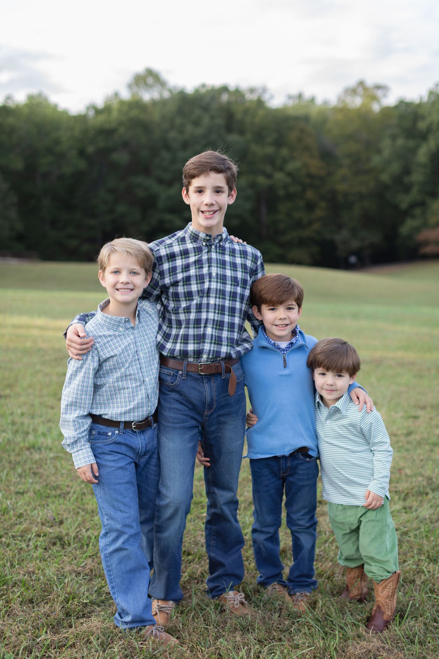 Four boys in coordinating outfits stand together in a grassy field during golden hour.