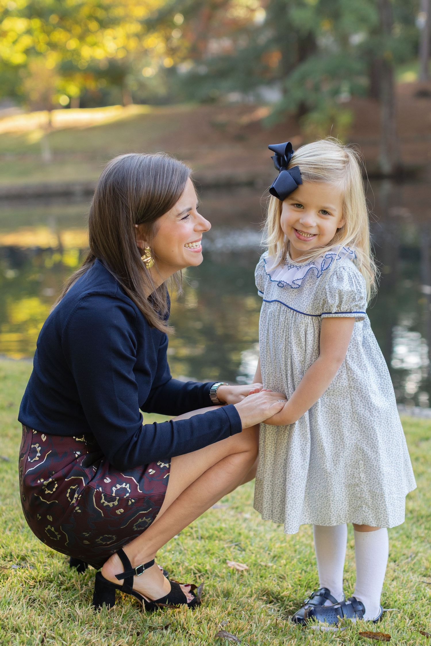 Mother and daughter share a tender moment together in a park setting by a pond during golden hour.