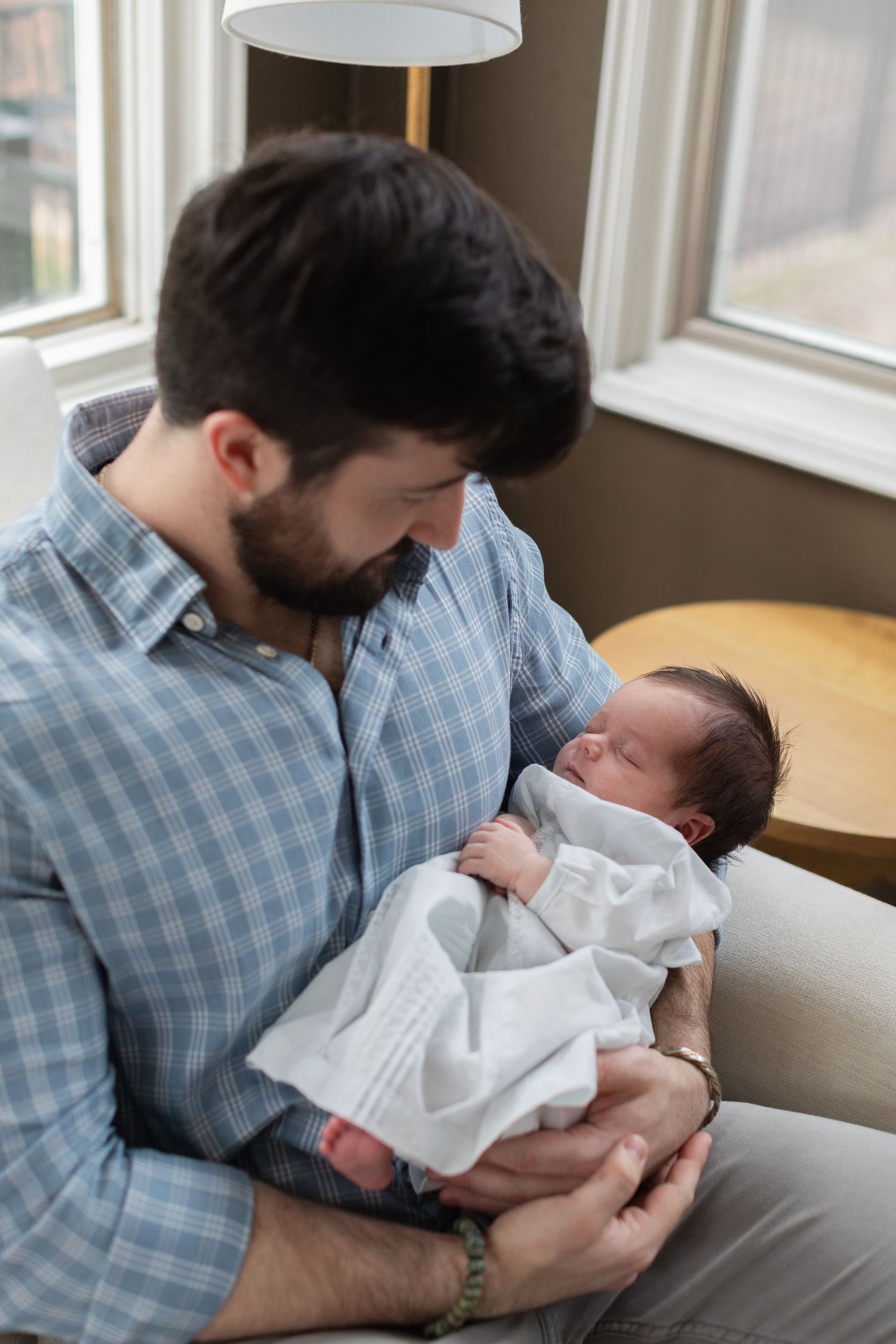 A gentle moment between parent and newborn baby under a modern pendant light.
