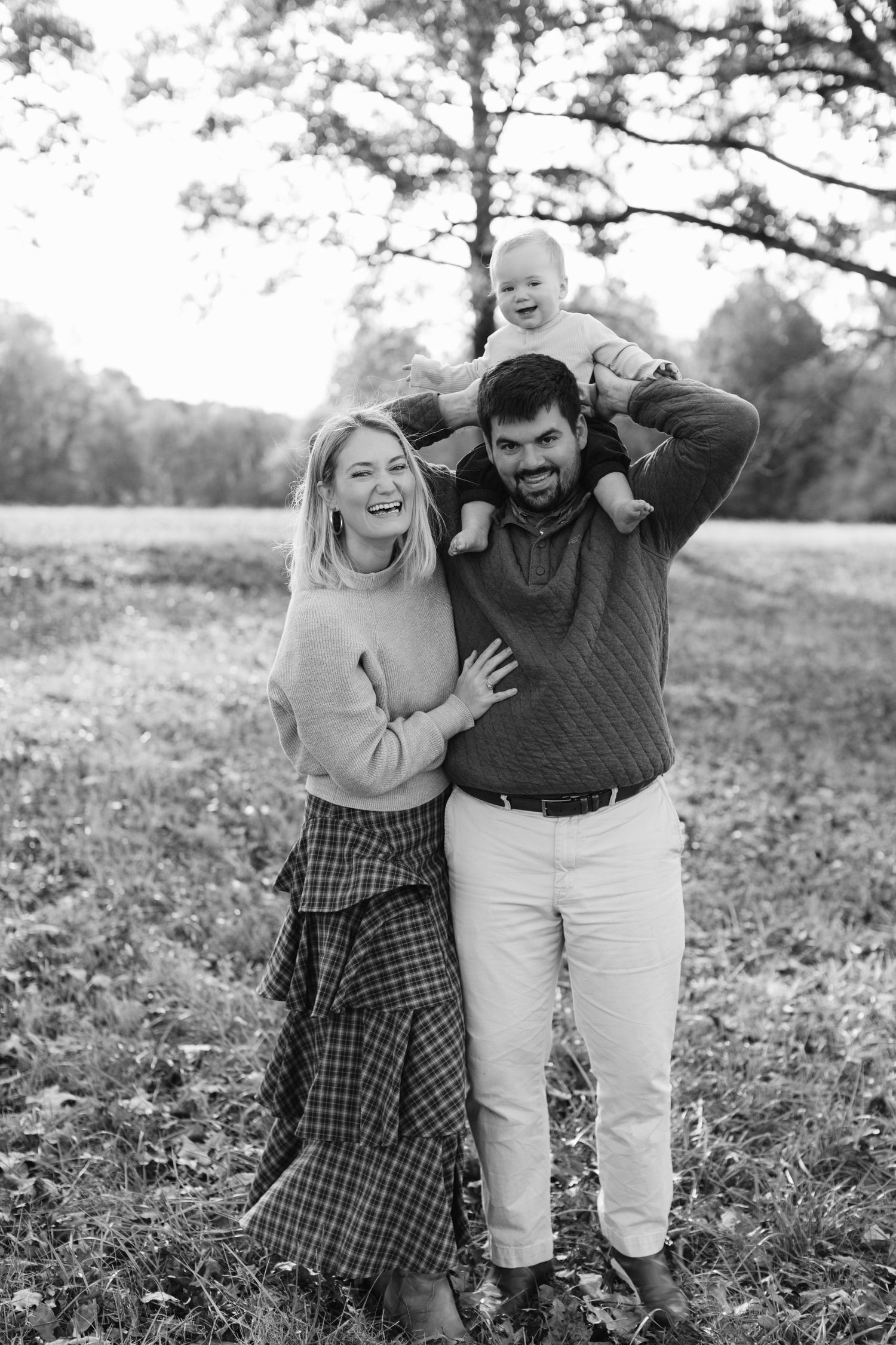 A couple laughs and embraces while enjoying a playful moment together in a grassy outdoor setting.