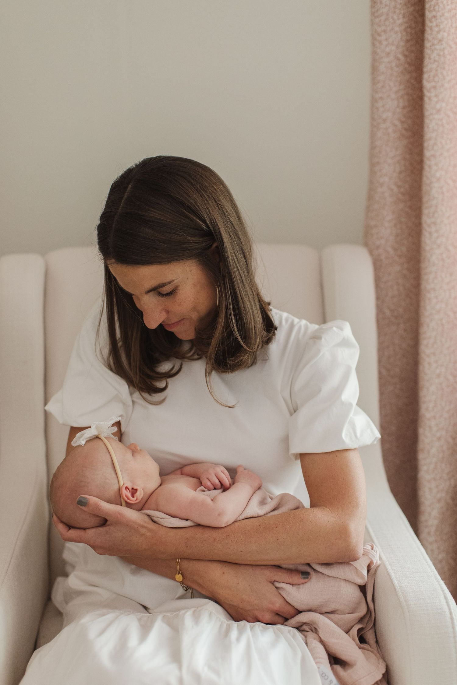 Mother tenderly embraces newborn on white bedding in natural lighting.