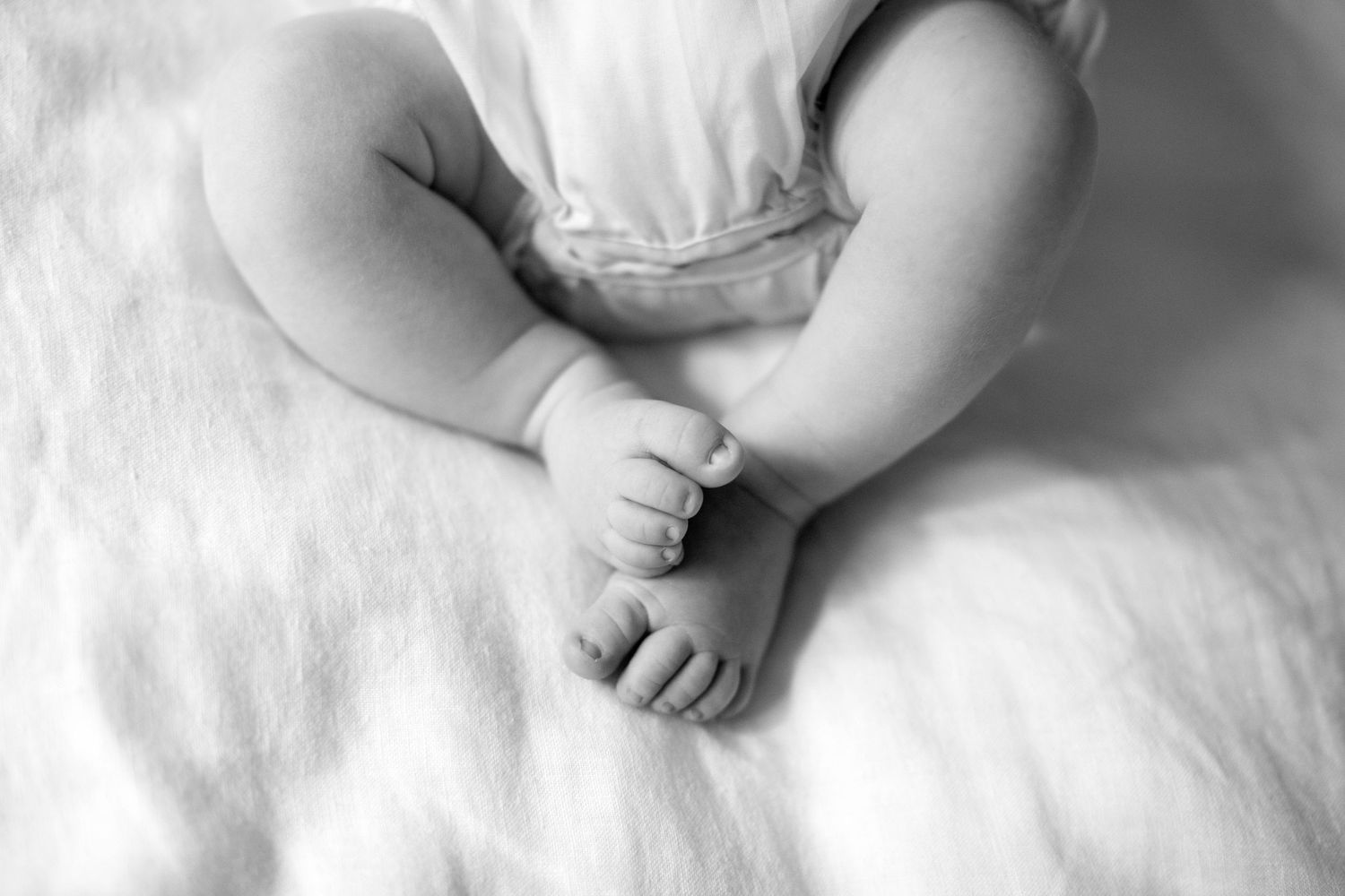 Infant wearing white clothing rests serenely against white cotton fabric.