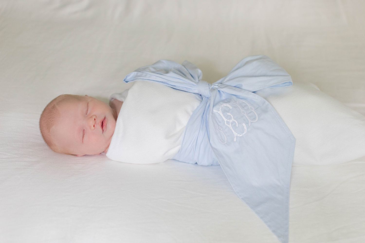 Sleeping baby in light blue and white outfit nestled on cream-colored textured bedding.