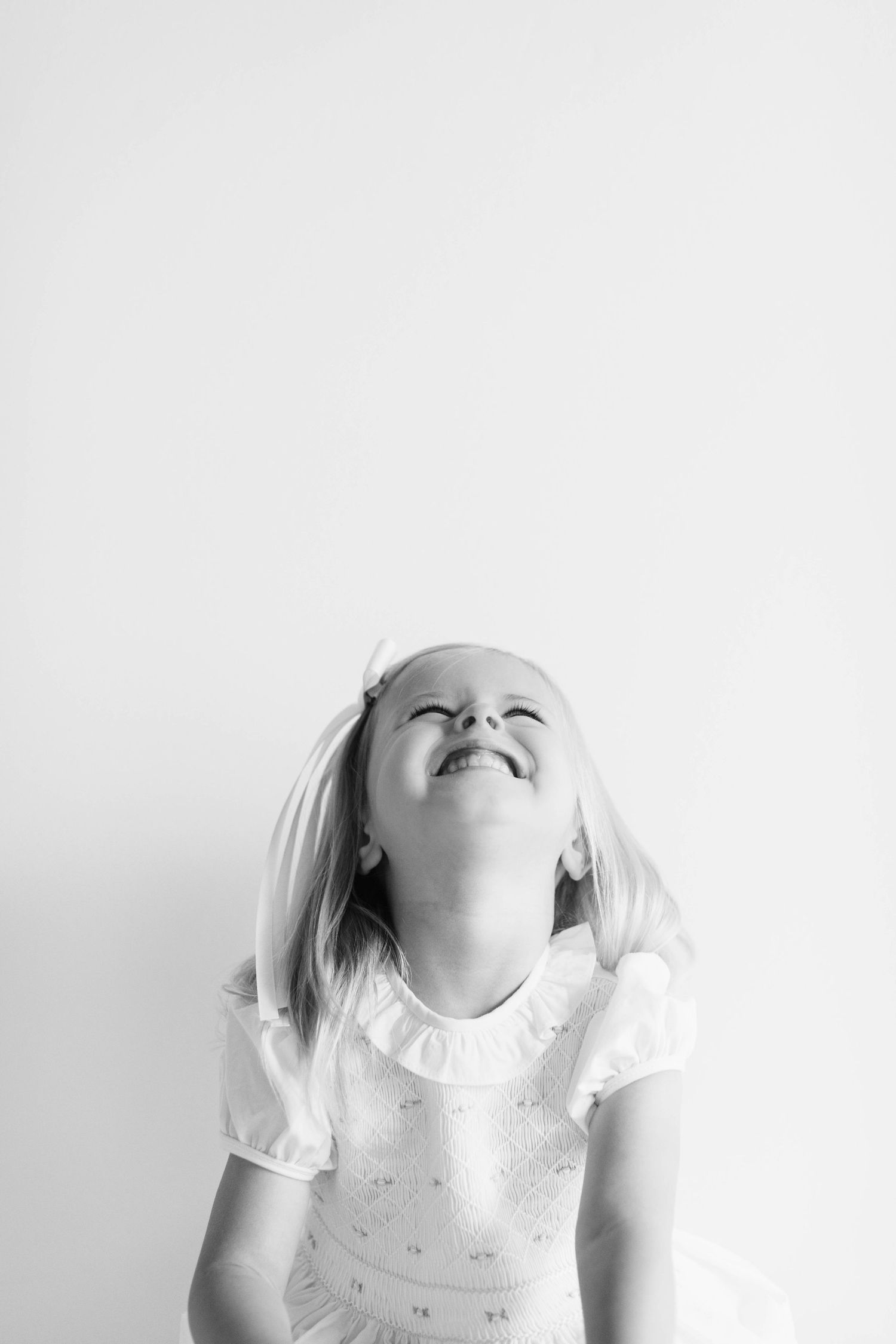 A sequence of joyful black and white photos showing a child in a white dress expressing pure happiness and laughter.