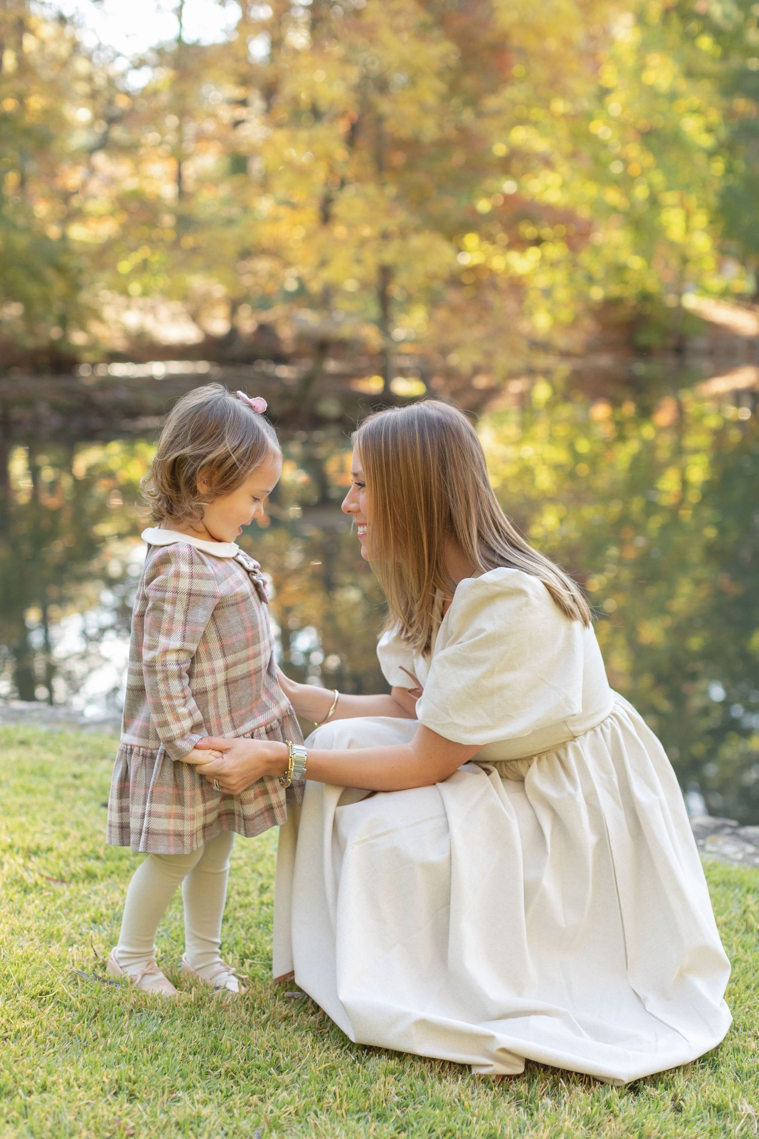 A tender moment between two people in a fall outdoor setting by a pond with golden autumn foliage in the background.