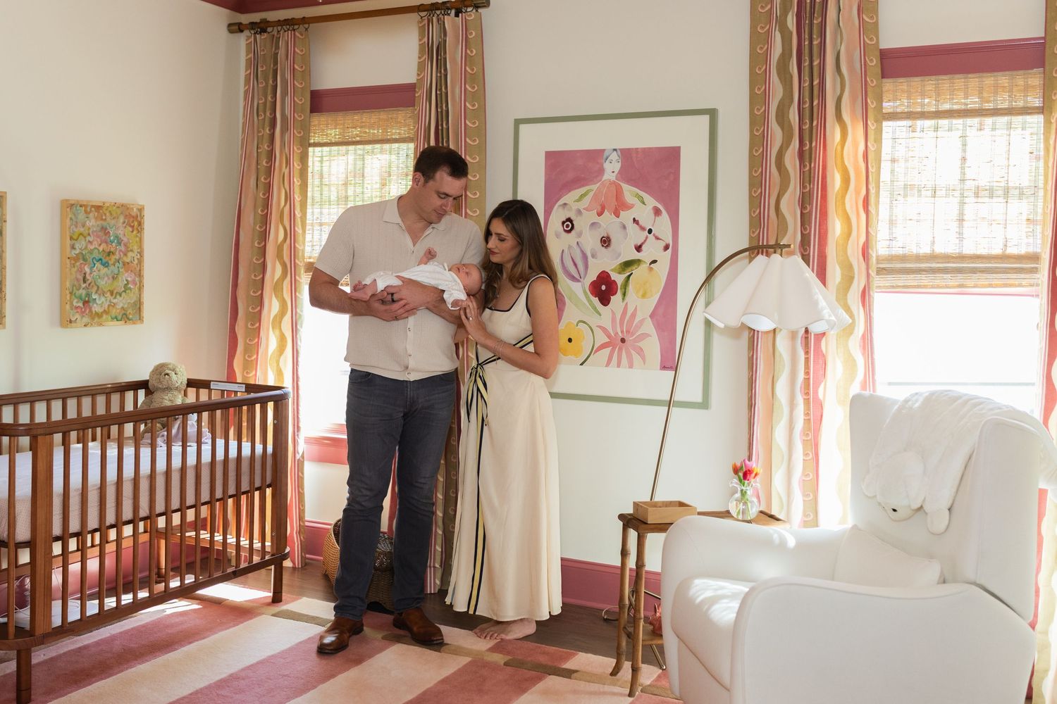 Couple admiring newborn in beautifully decorated pink nursery with crib and colorful curtains.