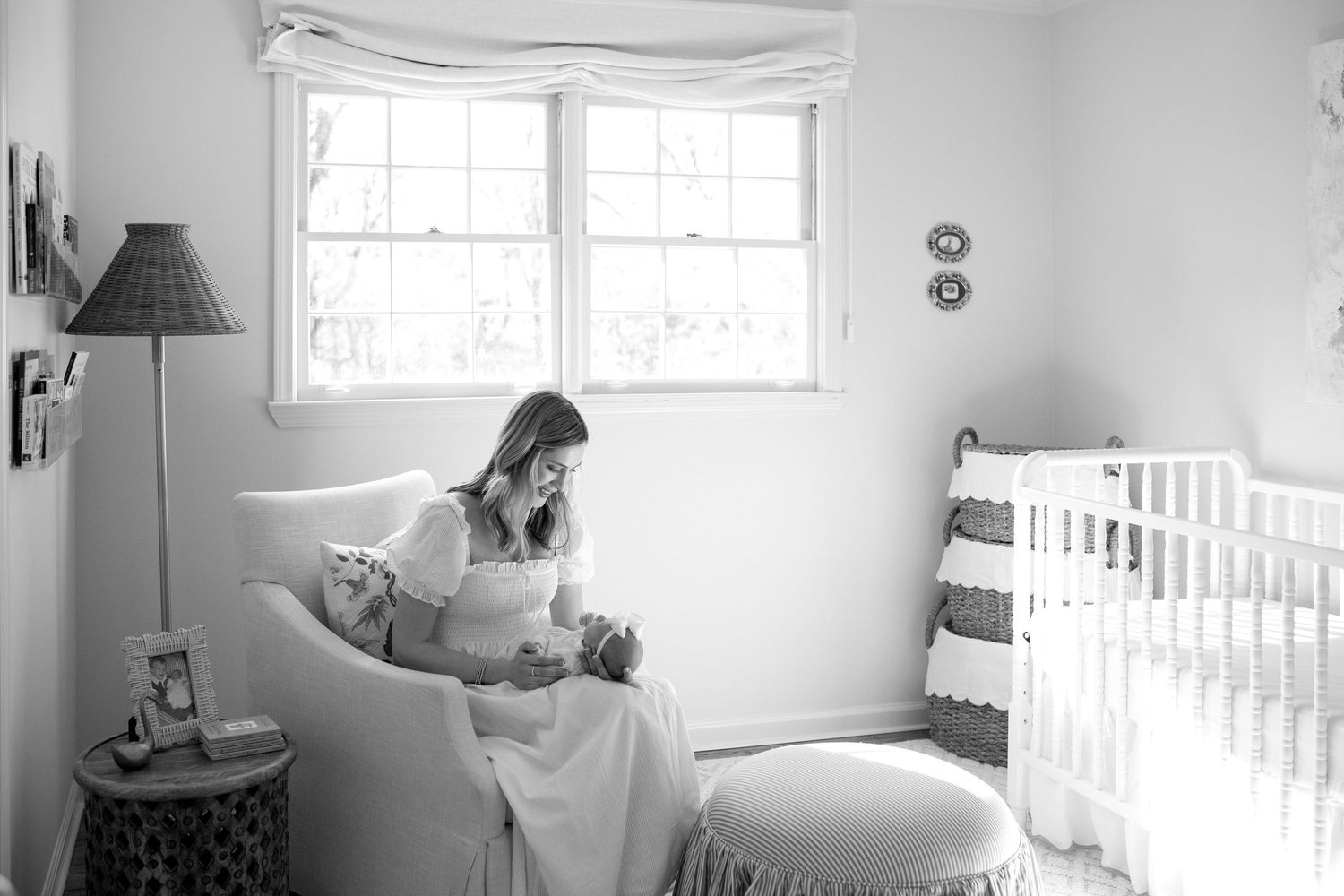 Black and white panoramic photograph shows a nursery room interior with a crib, lamp, and windows.