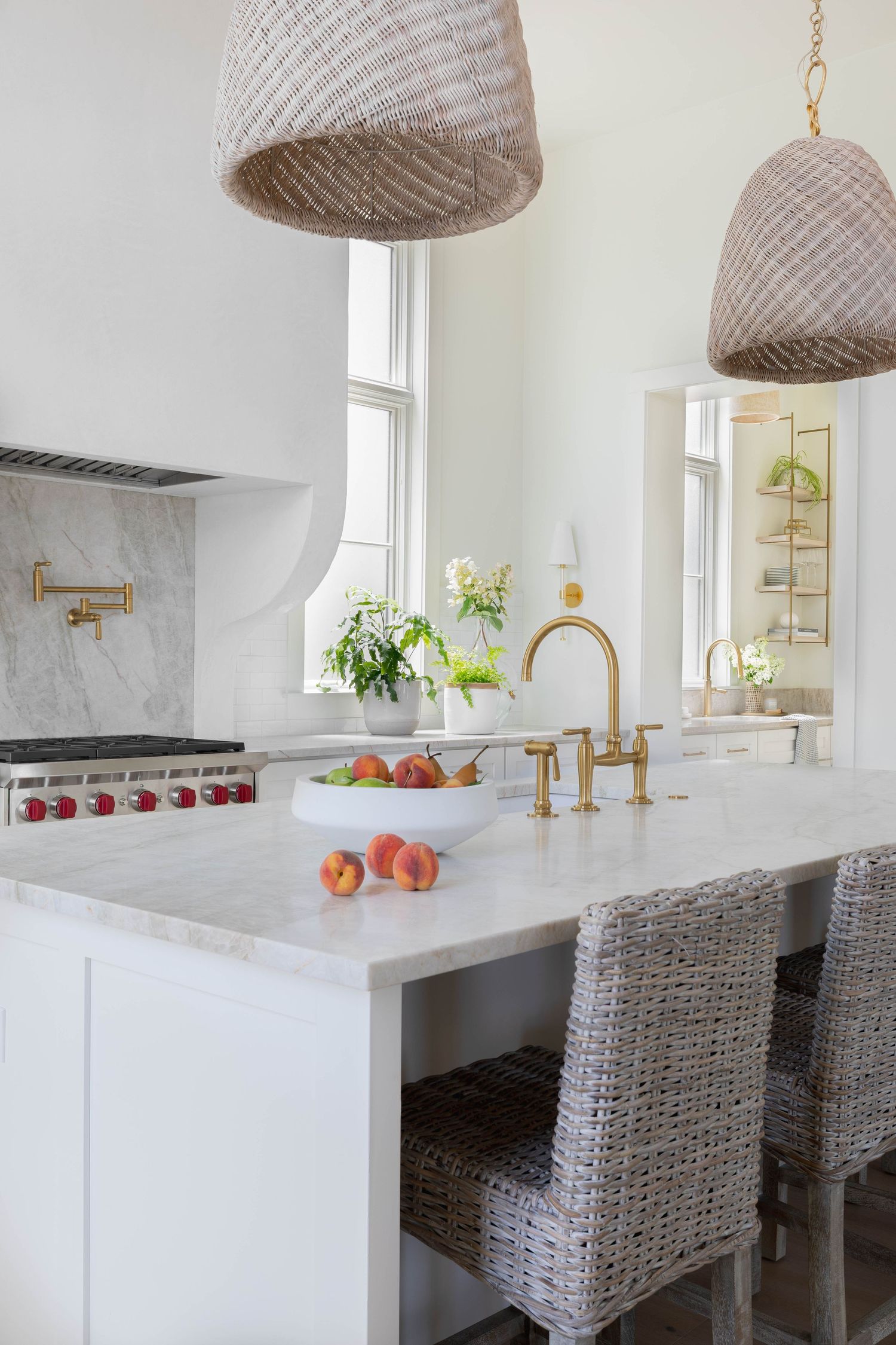 Modern white kitchen with marble counters, brass fixtures and woven pendant lights.