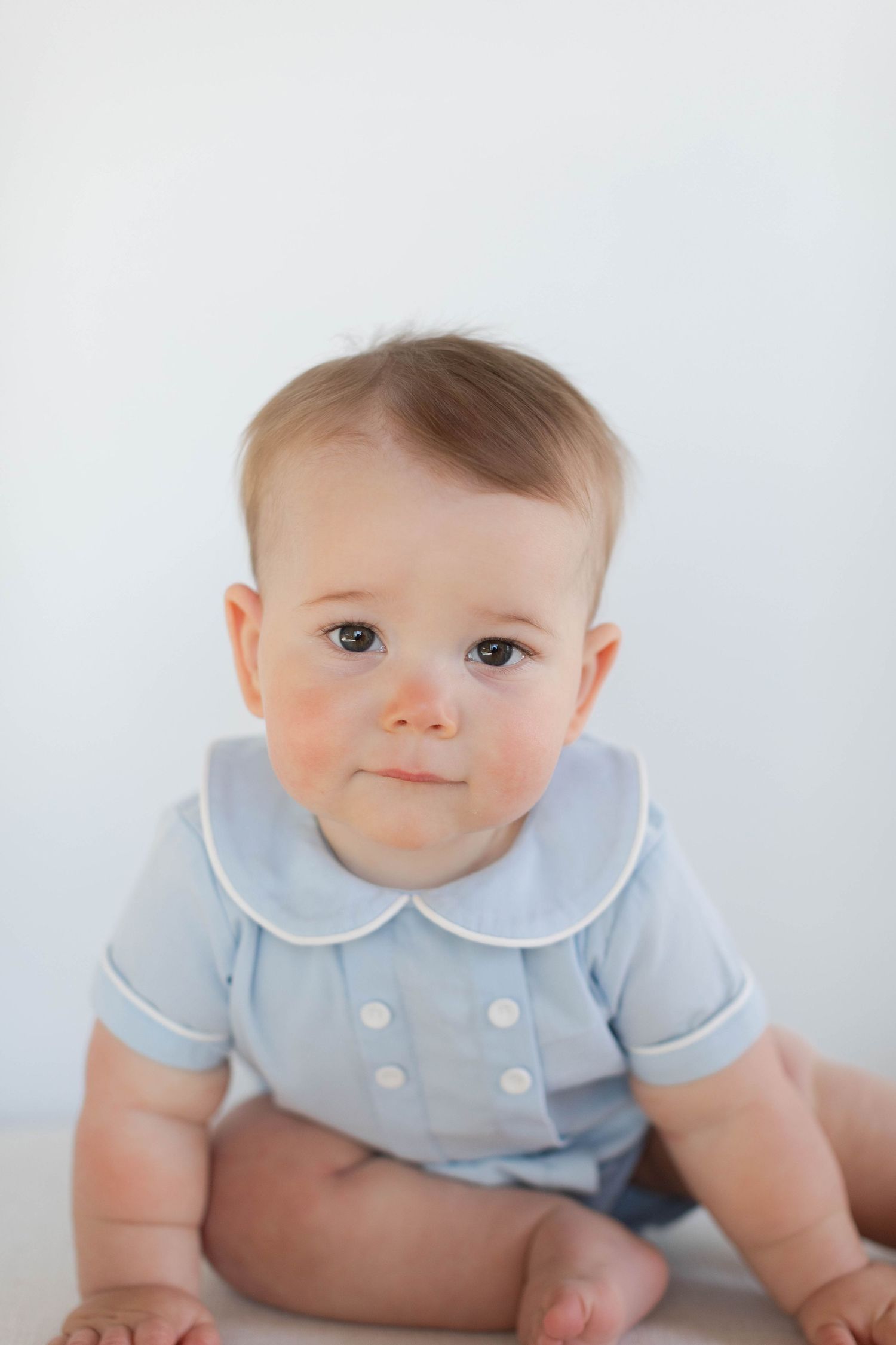 Baby wearing light blue outfit with peter pan collar sitting against white background.