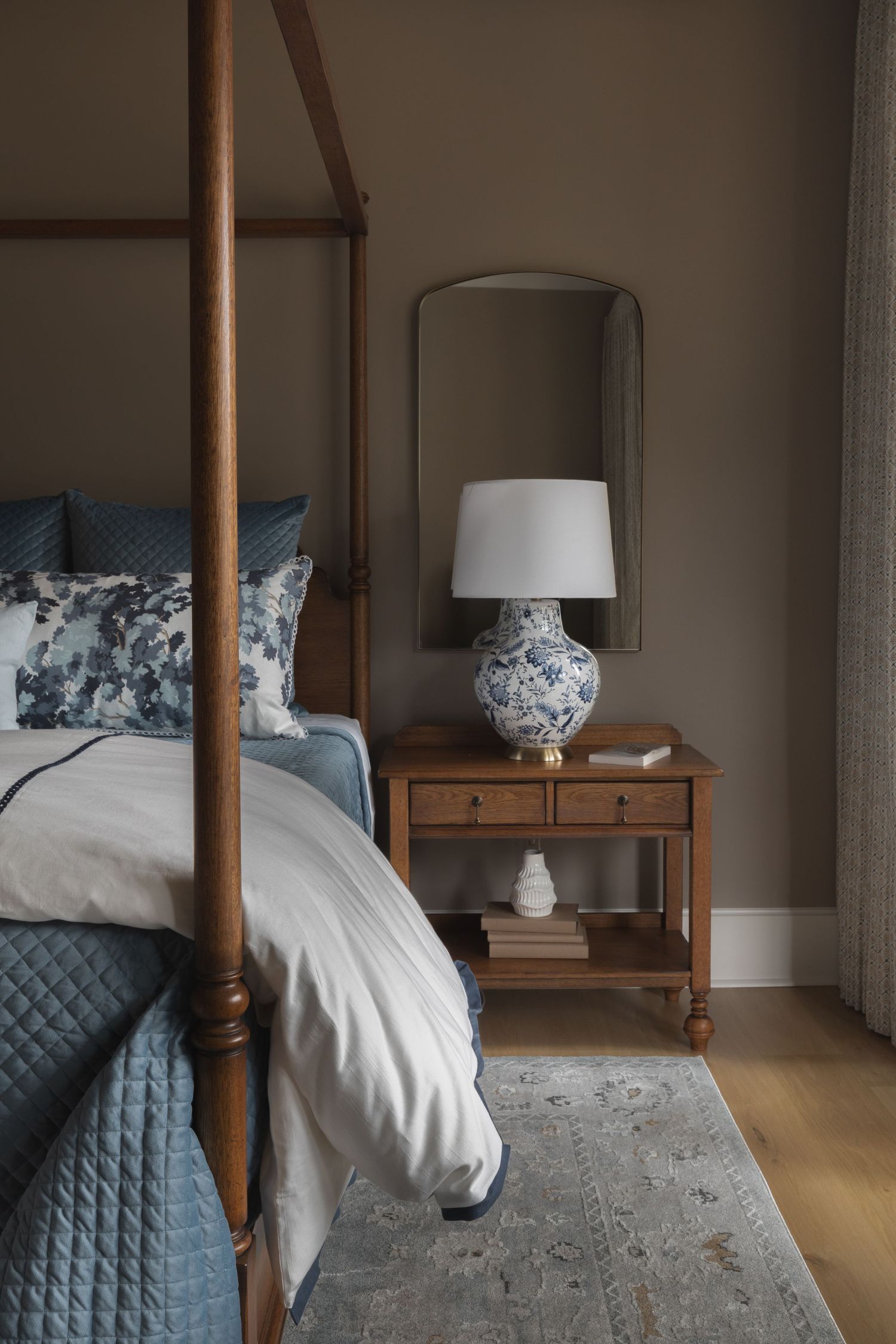 A cozy bedroom interior featuring a wooden four-poster bed with blue bedding and matching table lamps with floral patterns.